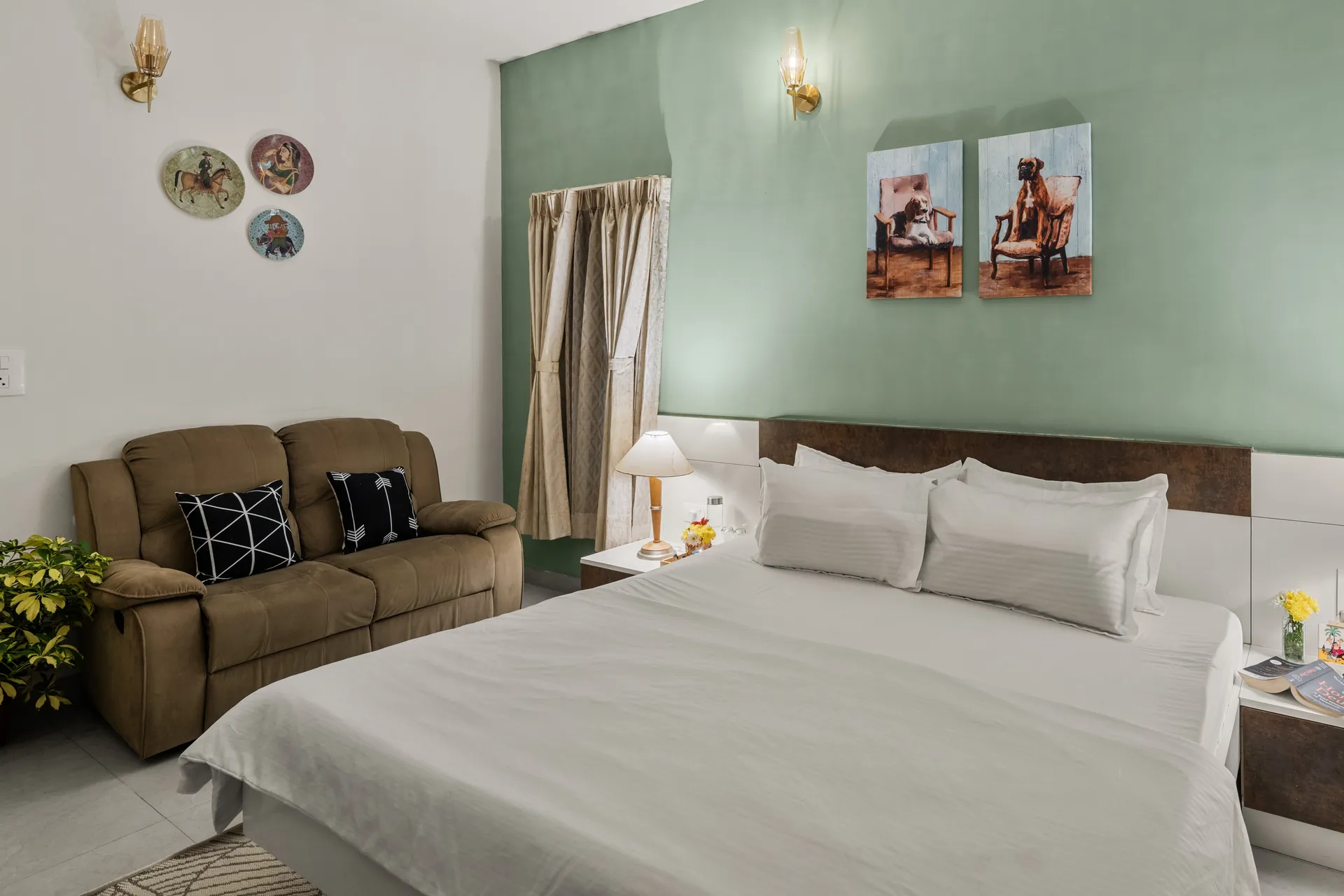 Bedroom with a made-up king bed, a brown recliner sofa, and two framed dog paintings on a sage green wall.