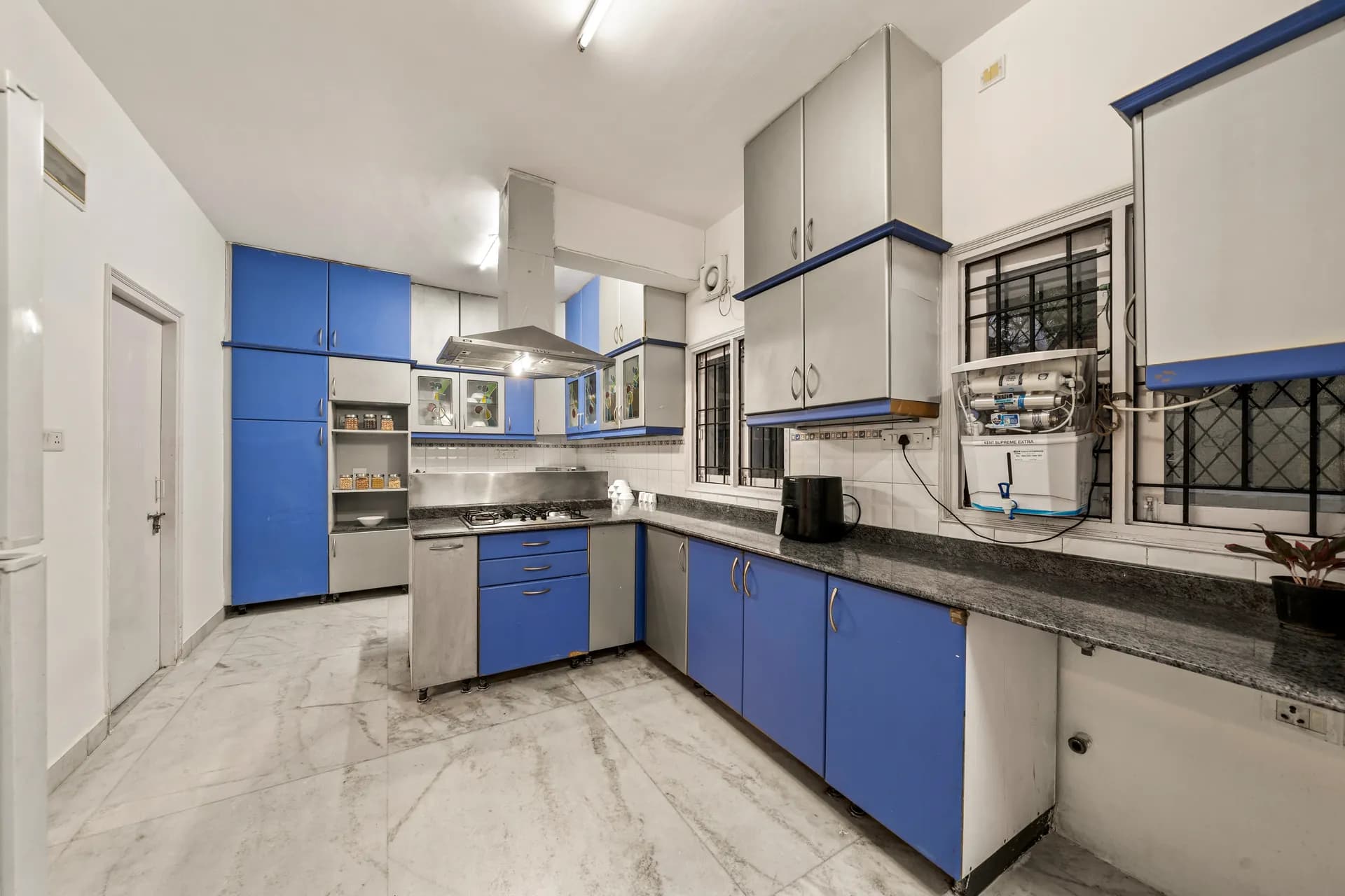 Galley-style kitchen with blue and grey cabinets, gas hob under extractor, dark granite counters and a water purifier.