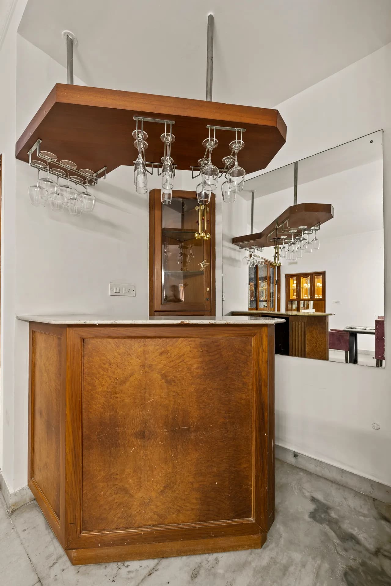 Indoor bar with a wooden counter, marble top, and wall-mounted rack holding wine glasses, with a mirror behind.