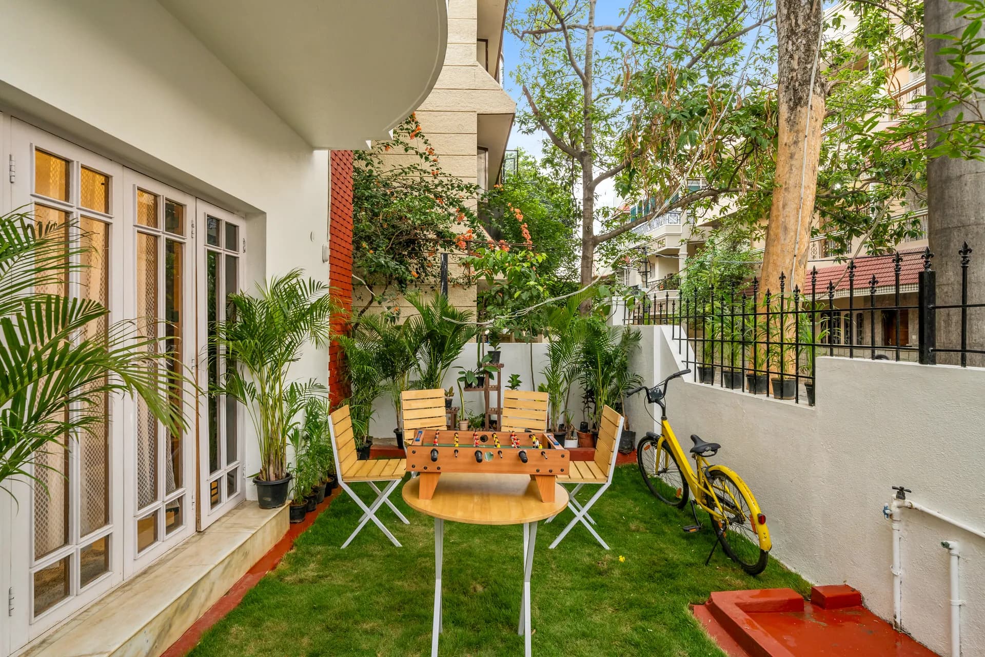 Grassy side garden patio with white French doors, a foosball table, wooden chairs and a yellow bicycle.