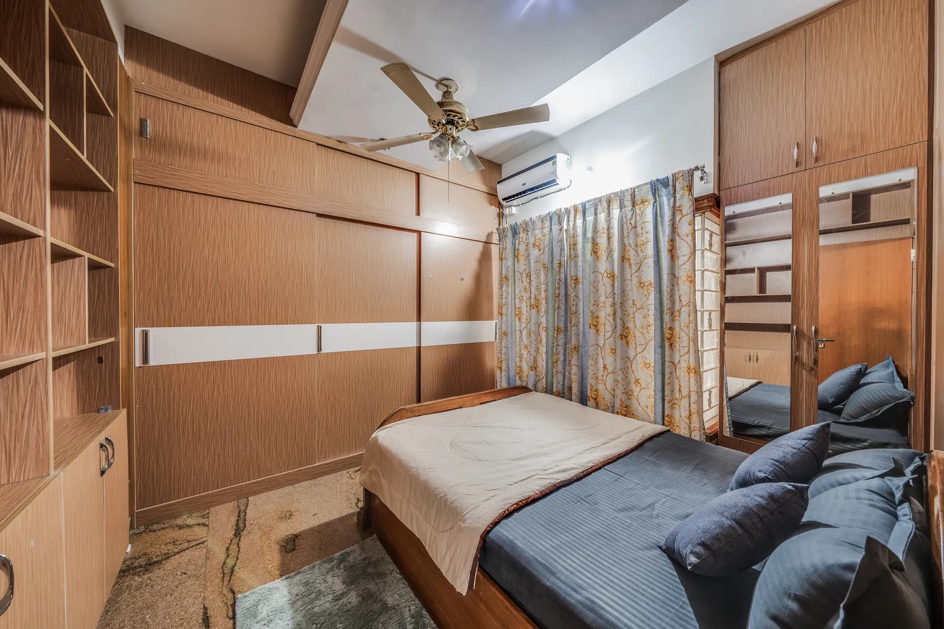 Bedroom with a double bed, wall-to-wall wooden wardrobes, a ceiling fan and an air conditioner.