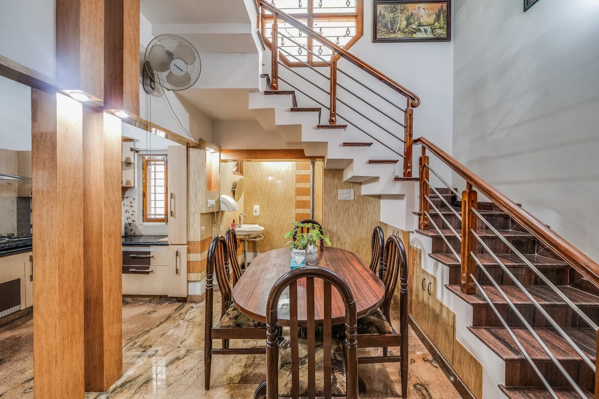 Dining area with a wooden table and chairs beside a staircase with wooden treads and metal railings.