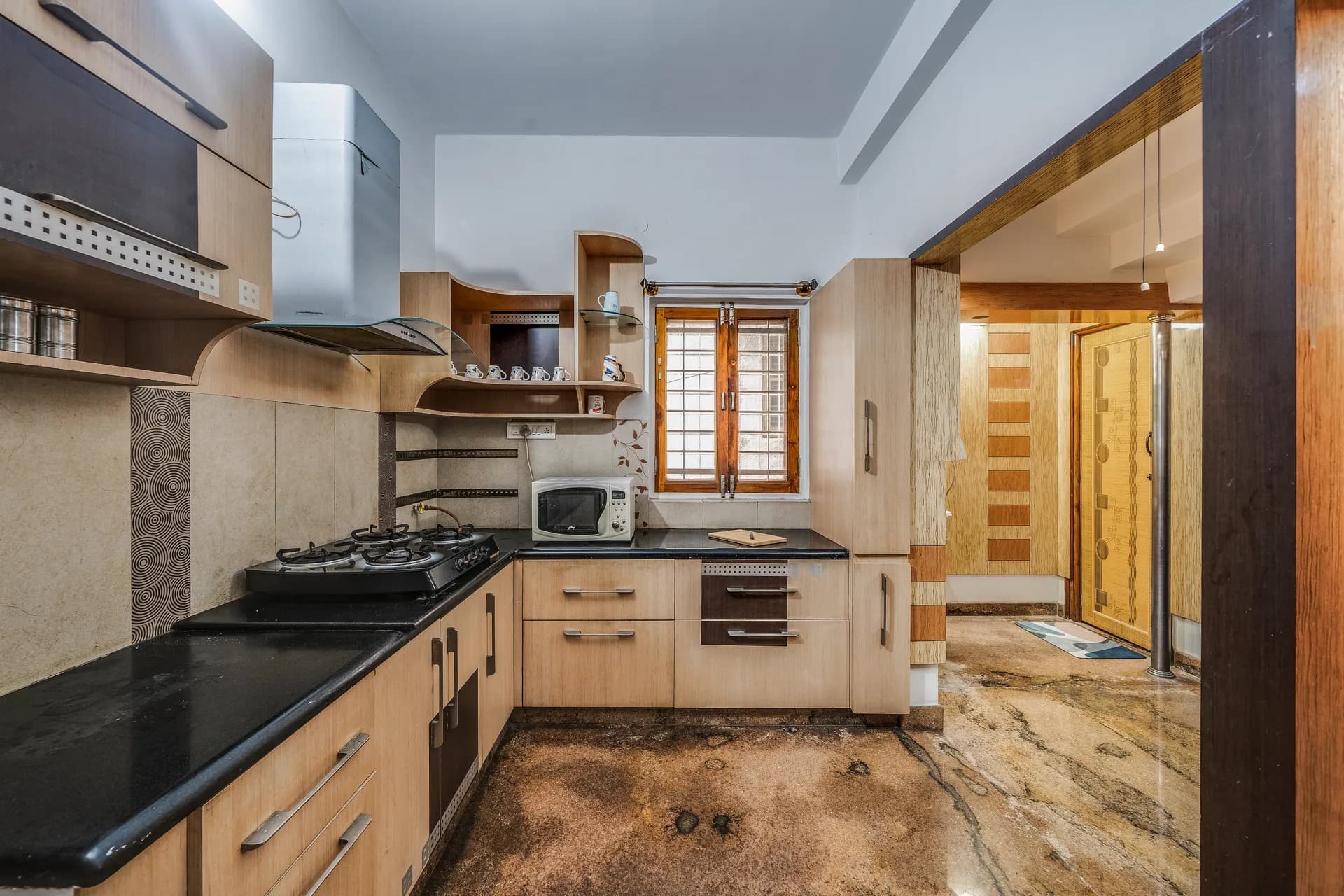 Compact kitchen with black countertops, four-burner gas hob, microwave and wooden cabinets beside a window.