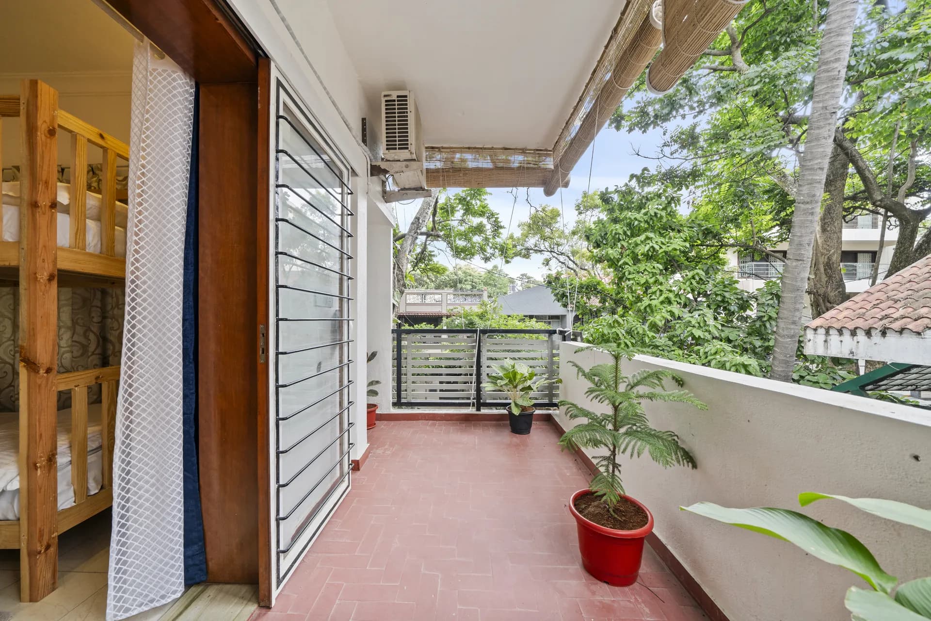 Narrow tiled balcony with bunk beds visible inside, potted plants and a view over leafy trees.