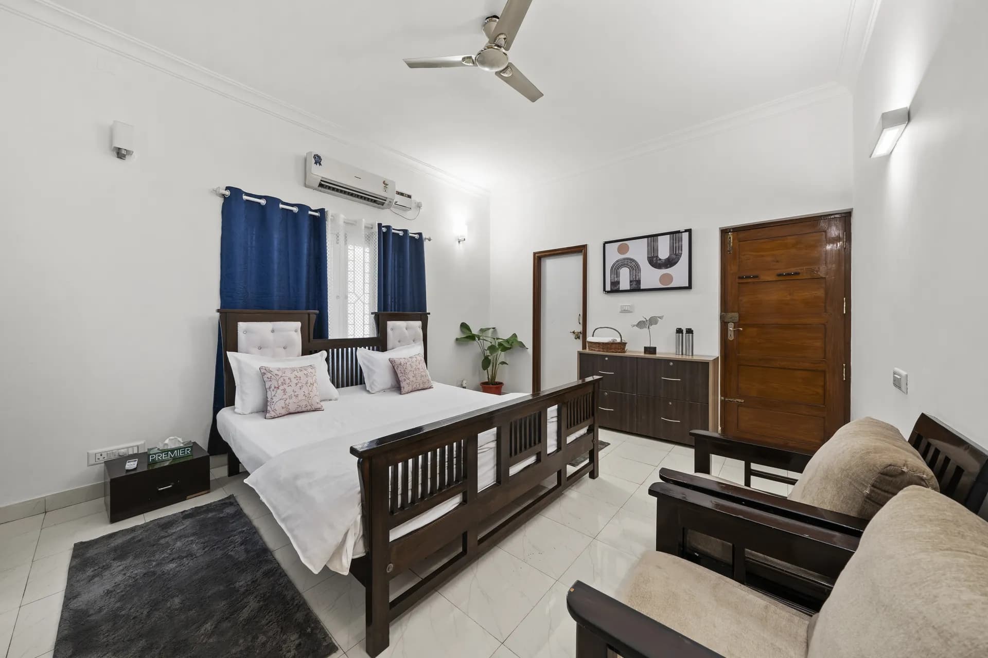 Bedroom with a double bed, navy curtains, wall air conditioner and a ceiling fan, plus two armchairs by the door.