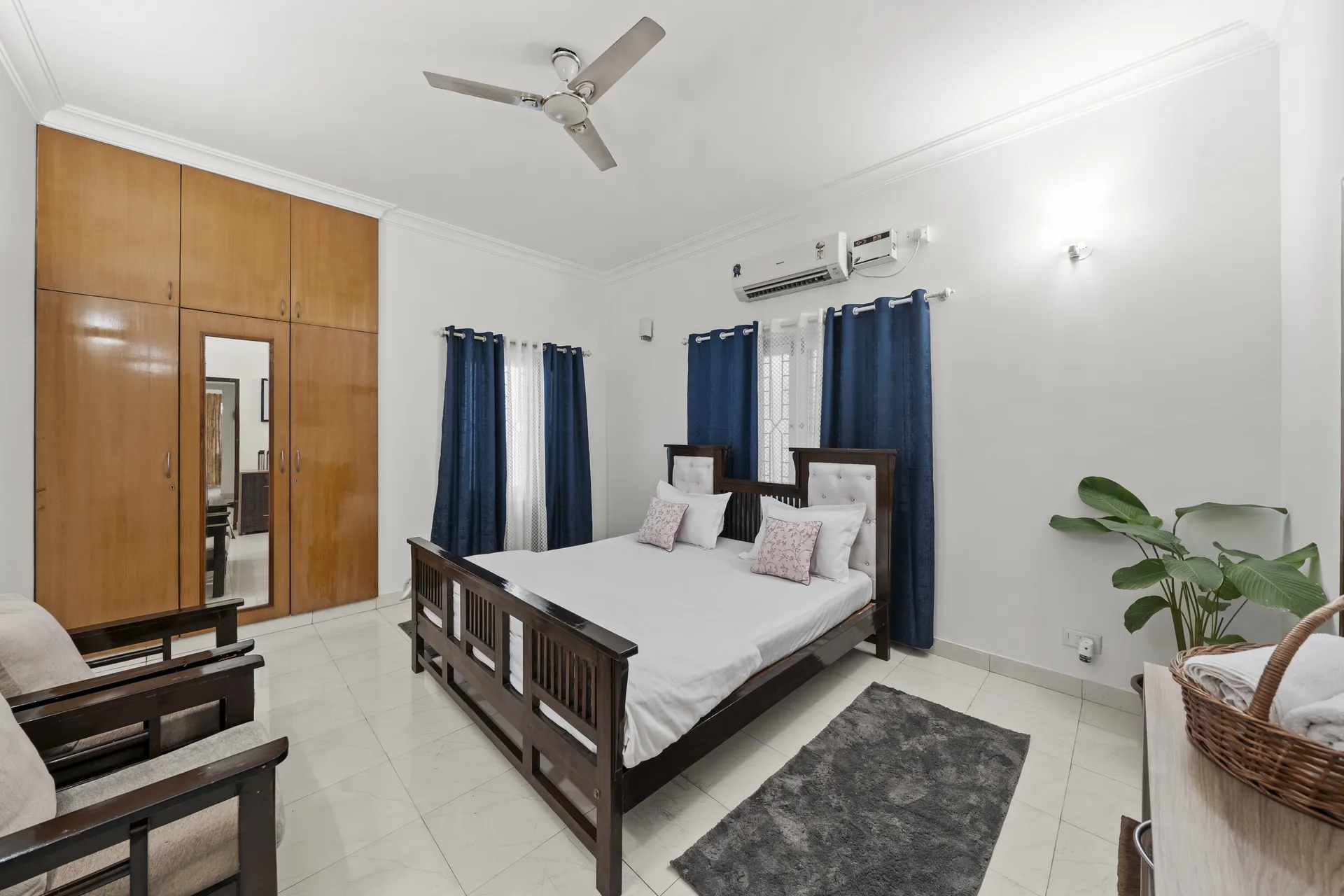 Bedroom with a made queen bed, blue curtains, built-in wooden wardrobe and a wall-mounted air conditioner.