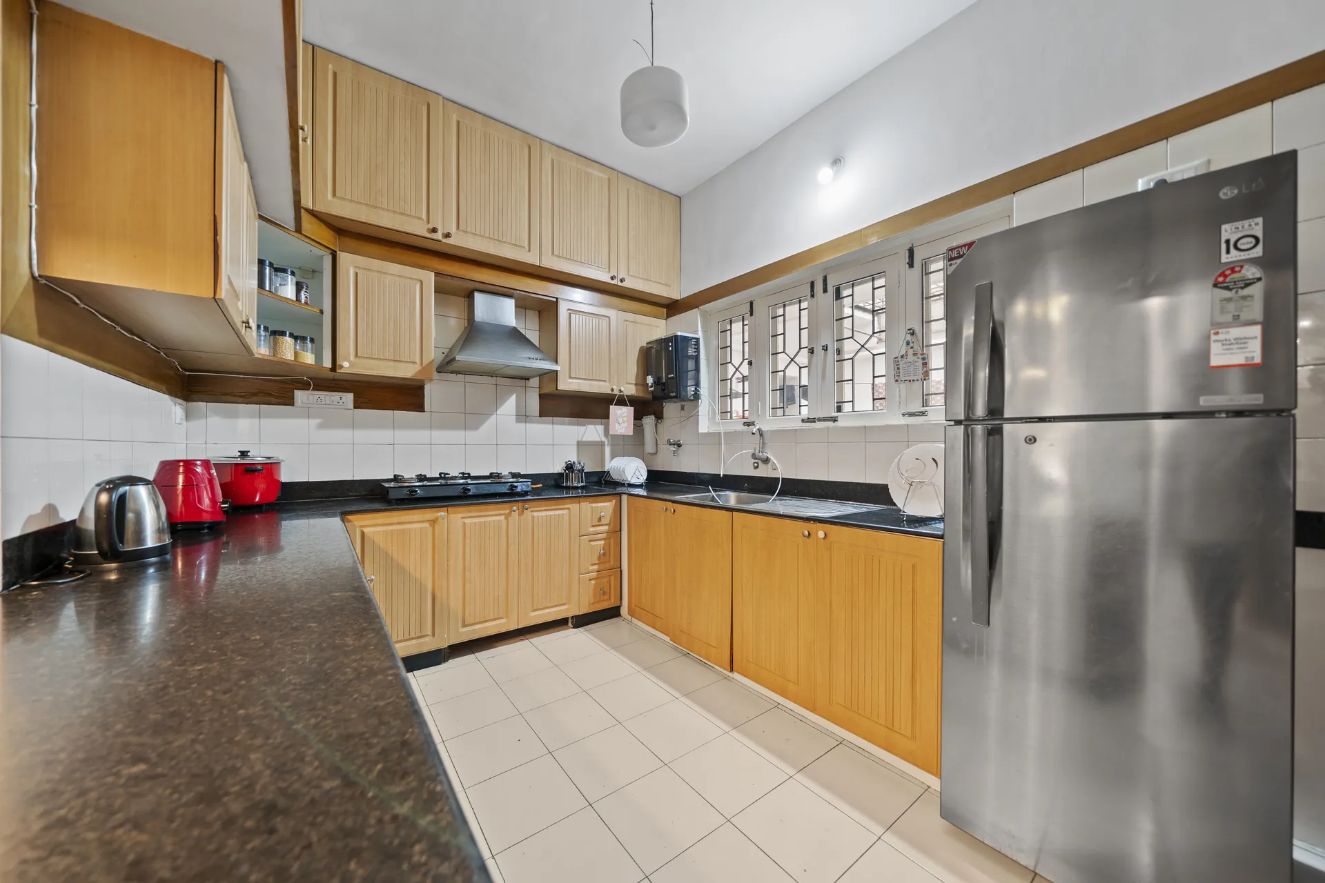 Galley-style kitchen with wooden cabinets, dark countertops, a gas hob, steel fridge and red kettle and pan.
