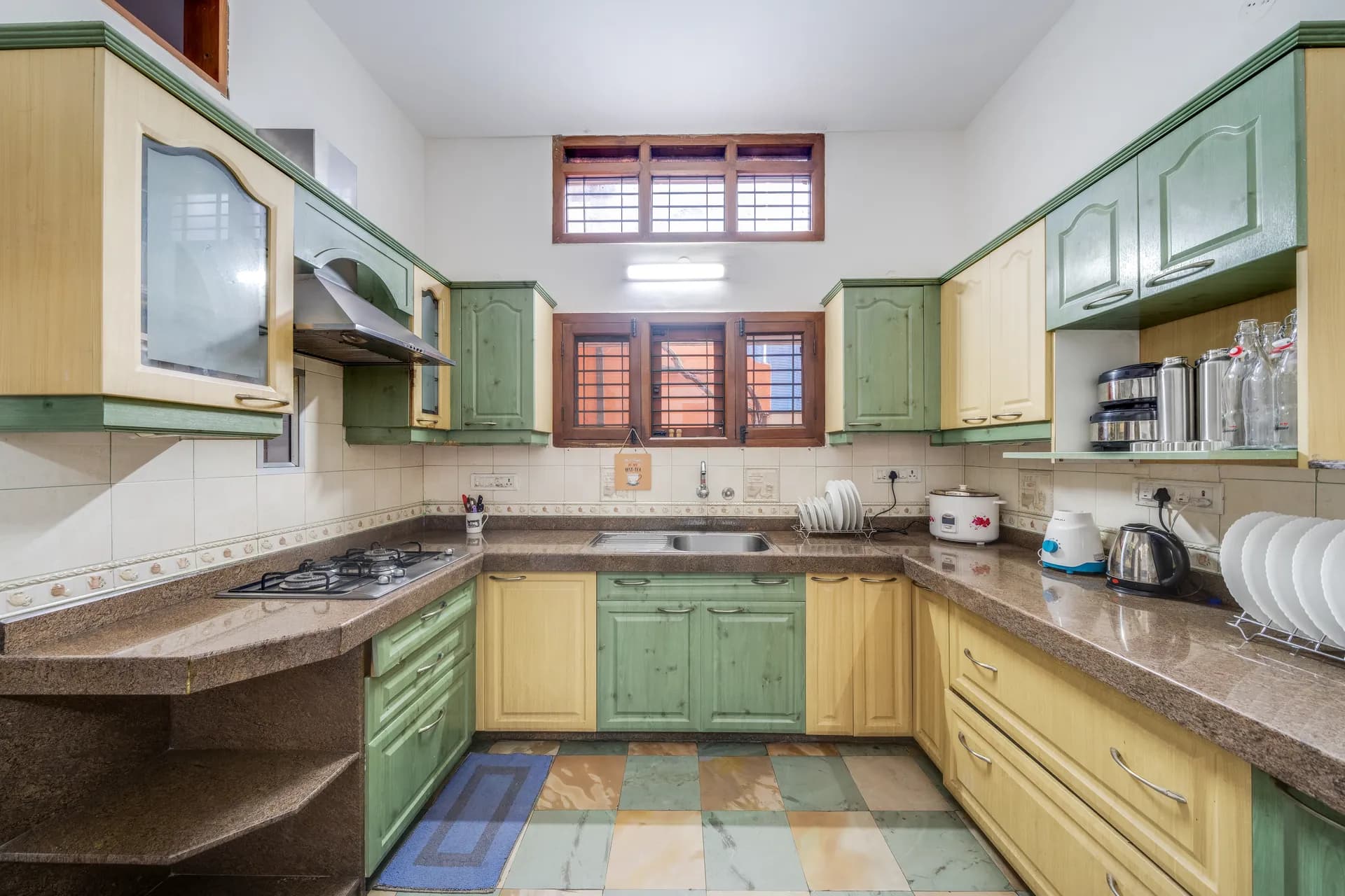 Kitchen with two-tone green and cream cabinets, gas hob, steel sink and a row of appliances on the counter.