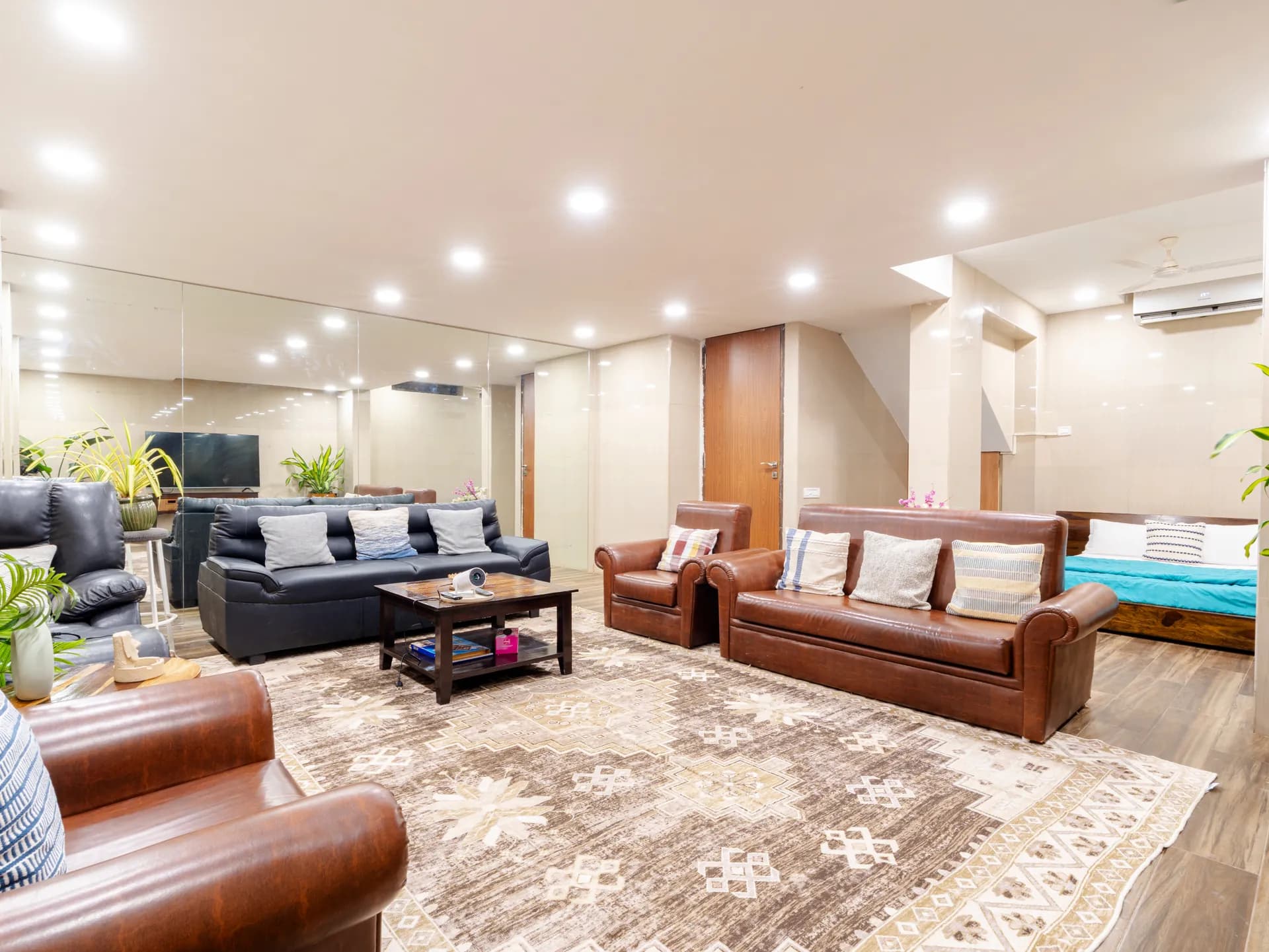 Large lounge with two leather sofas, a dark sofa, a patterned rug and a bed in the corner.
