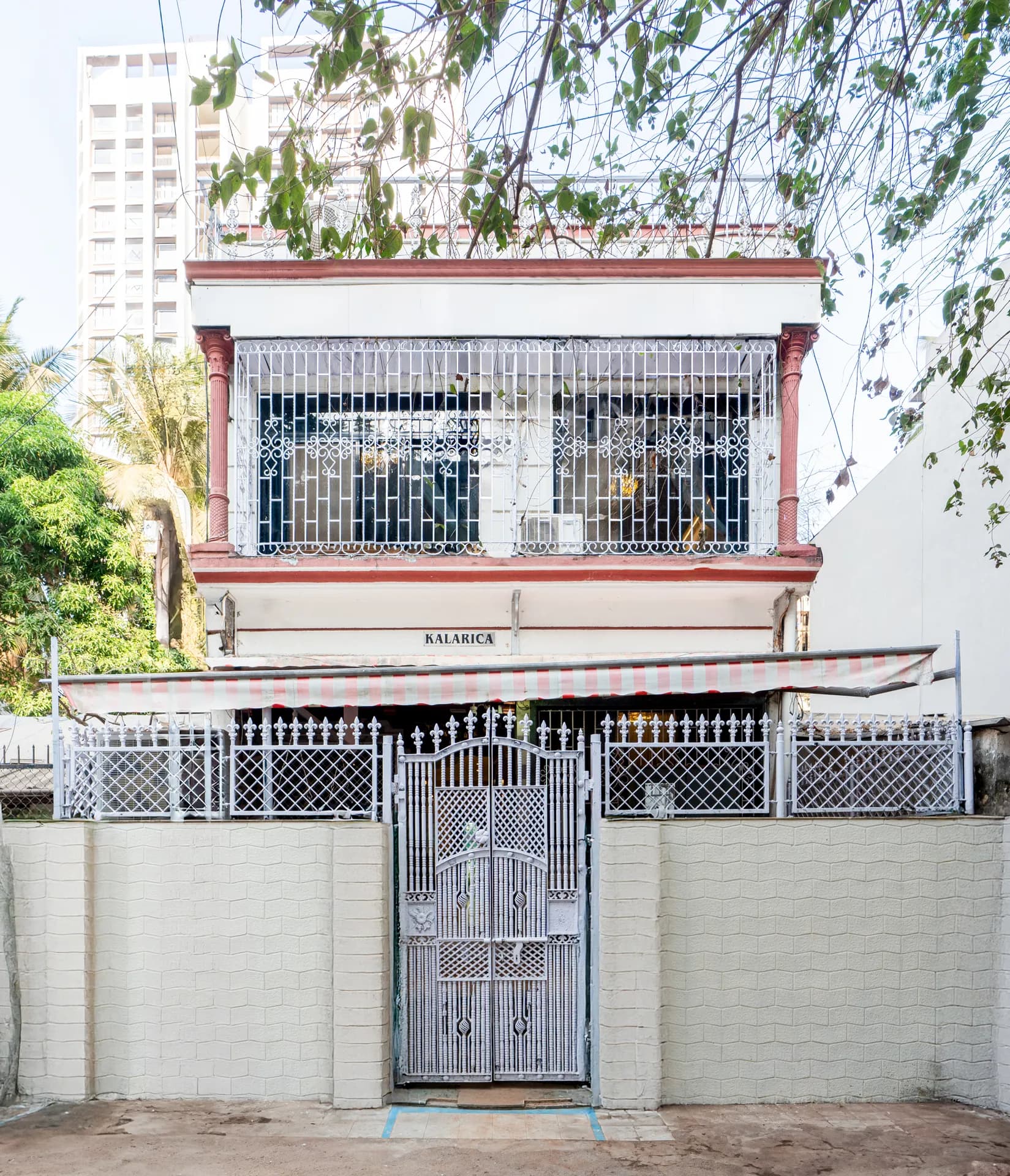 Front facade of a two-storey house behind a white gate and fence, with a striped awning and a KALARICA nameplate.