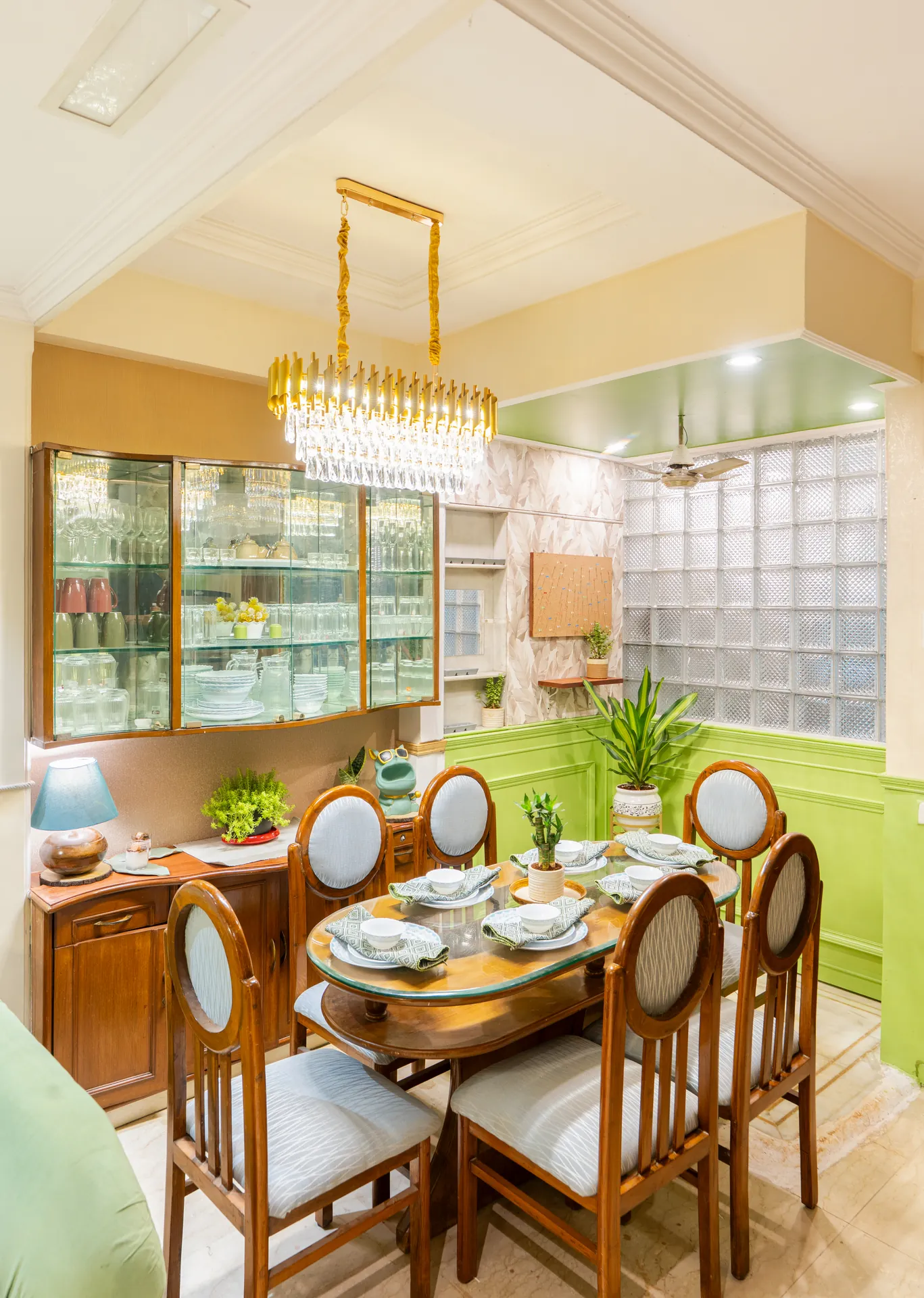 Dining area with a six-seat oval wooden table, glass-fronted display cabinet and a gold crystal chandelier.