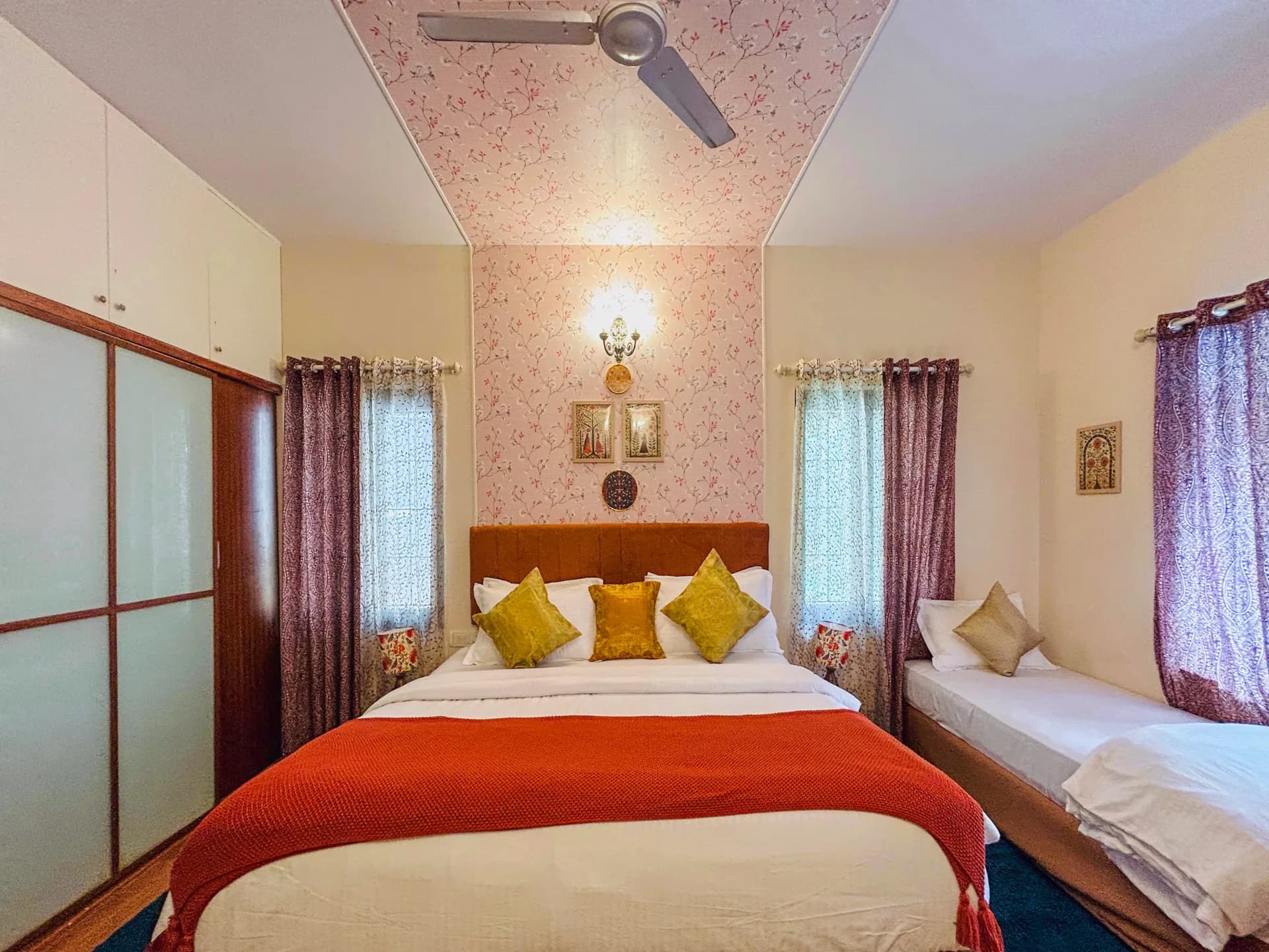 Bedroom with a double bed, a single bed, a ceiling fan and a built-in wardrobe under pink floral wallpaper.