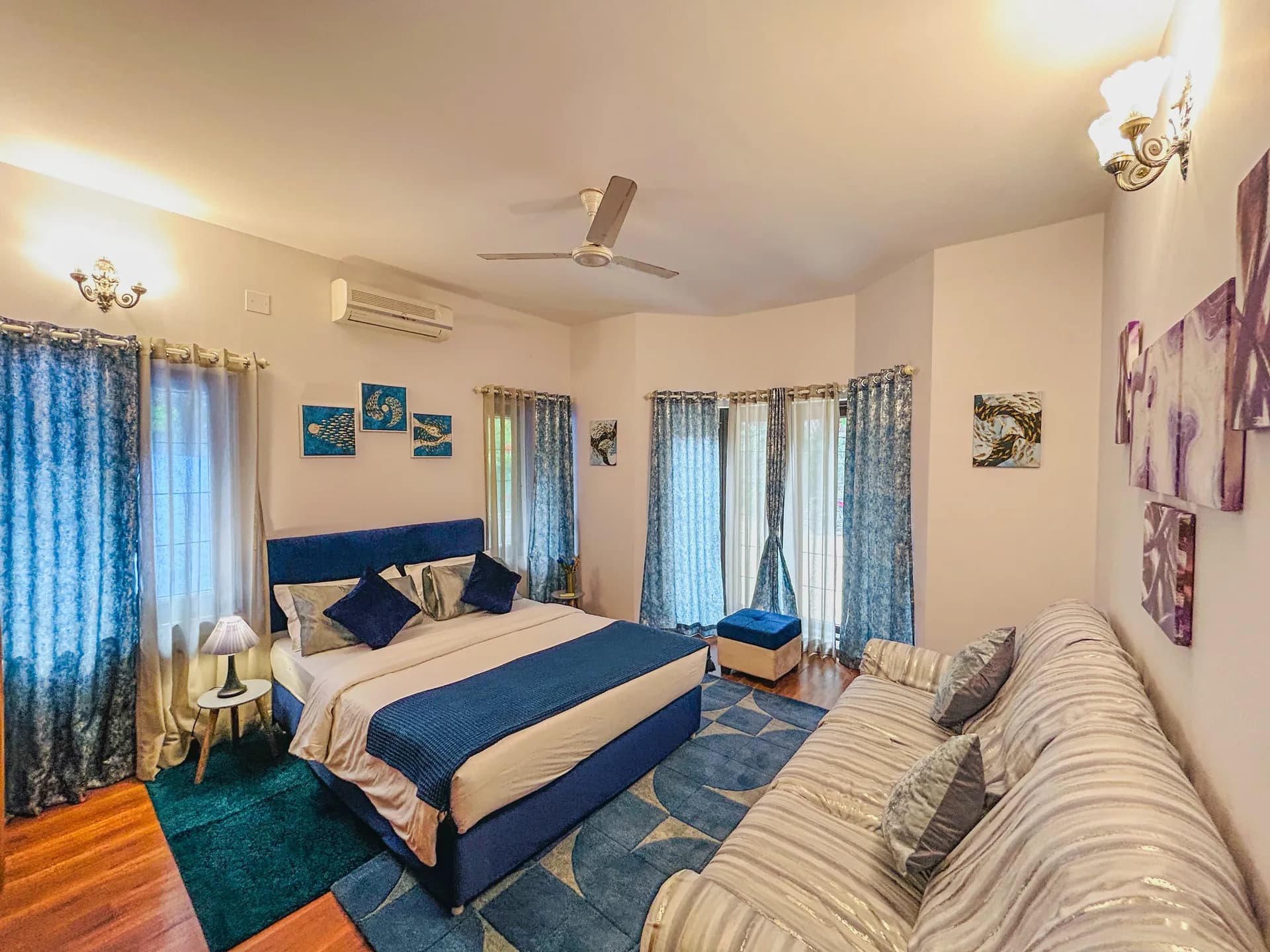 Bedroom with blue upholstered bed, blue curtains, wall air conditioner and a ceiling fan.