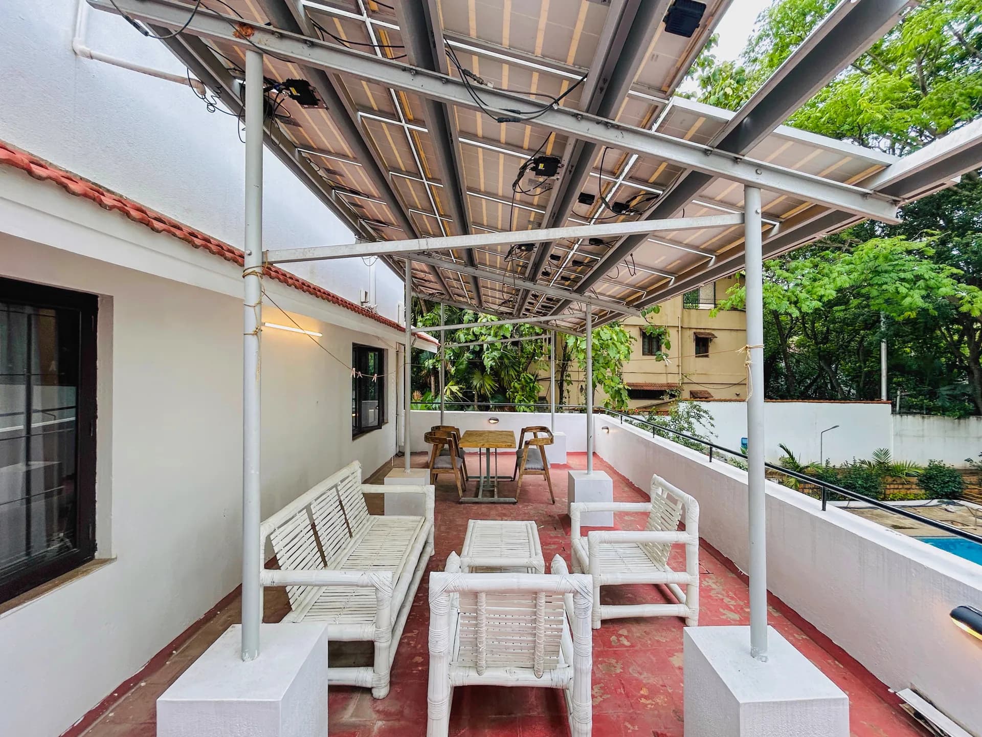 Covered terrace with white cane seating, a wooden dining table, and a pool edge visible beside it.