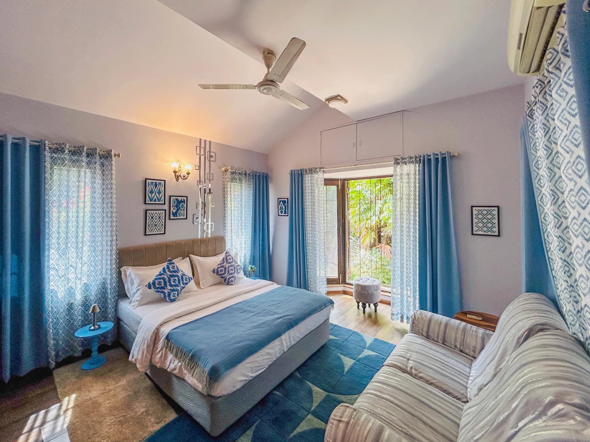 Bedroom with a double bed in blue bedding, blue patterned curtains, and a glass door opening onto greenery.