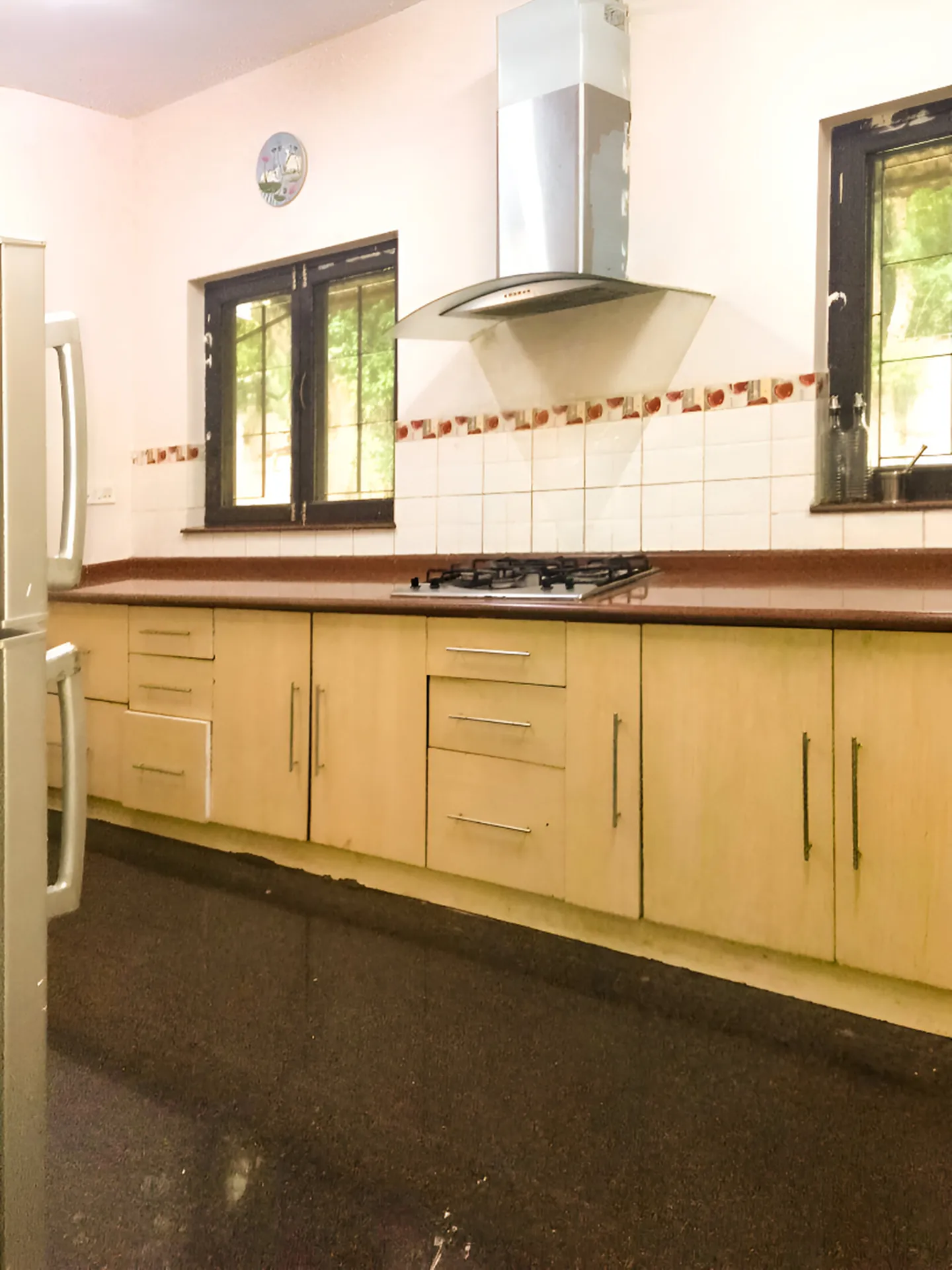 Kitchen with pale wood cabinets, a gas hob under a stainless steel hood, and two windows over the counter.