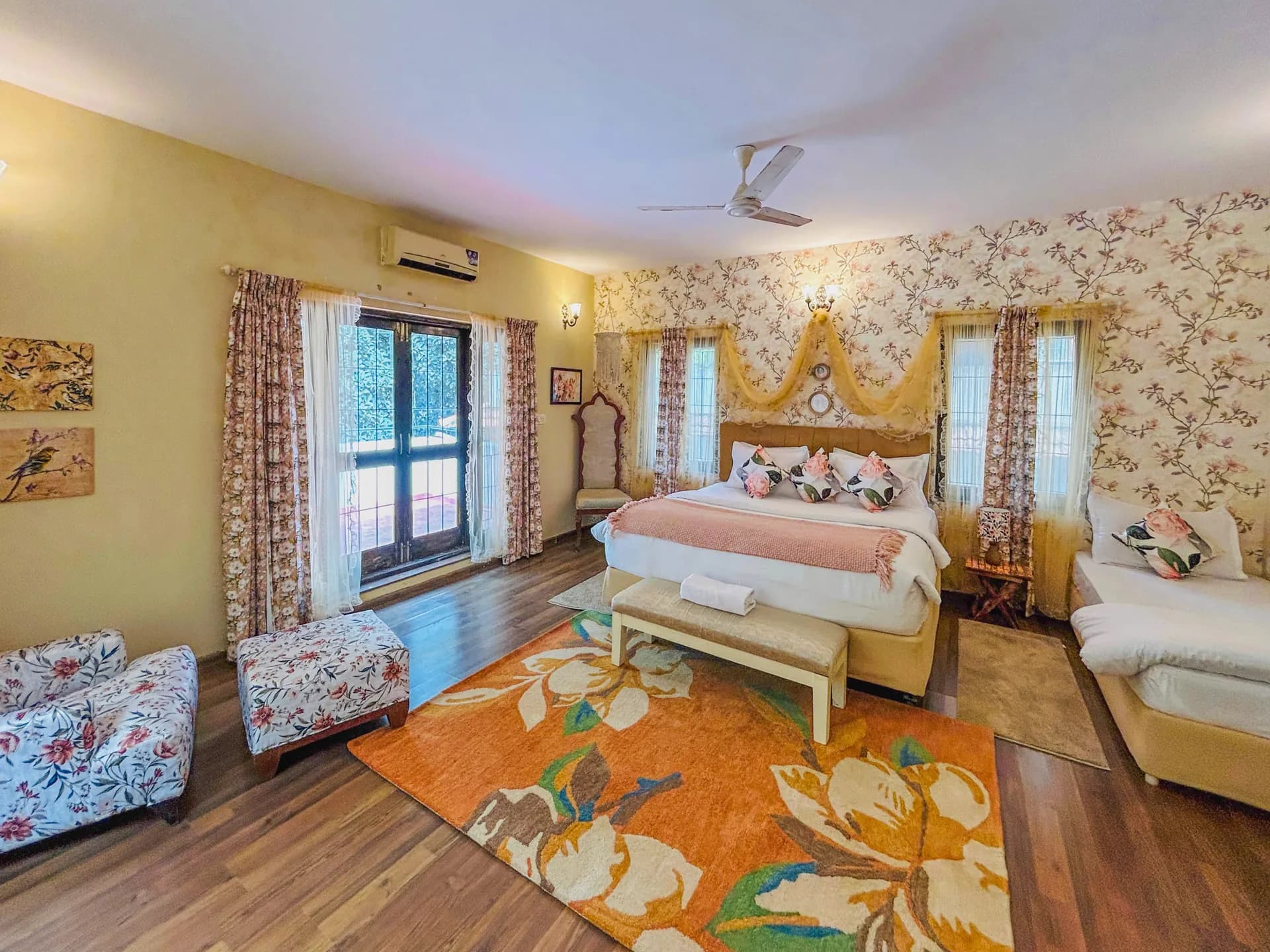 Bedroom with a king bed under floral wallpaper, a single bed to the right, and an orange floral rug on wood floors.