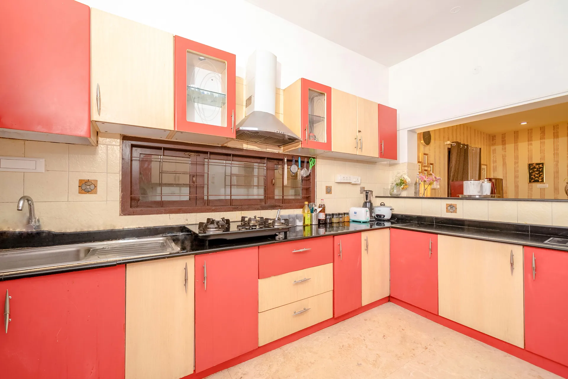 Bright kitchen with red and cream cabinets, black countertops, a gas hob and stainless sink.