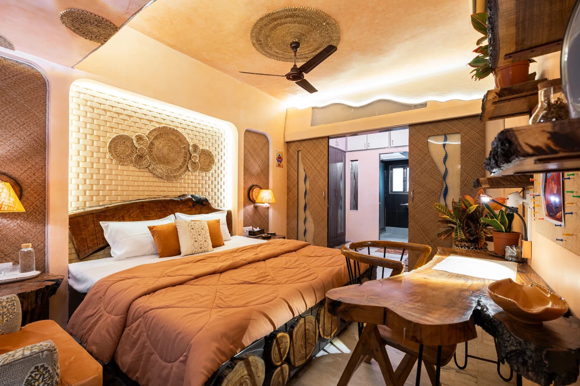 Bedroom with a king bed under a woven headboard wall, a live-edge wooden desk, and a ceiling fan.