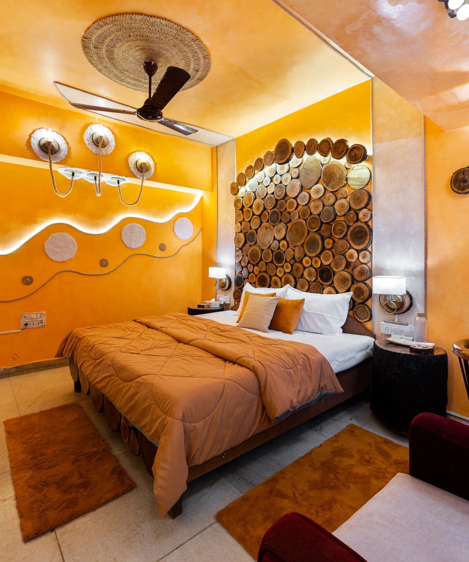 Bedroom with a king bed, orange walls, and a headboard made of stacked wooden log slices.