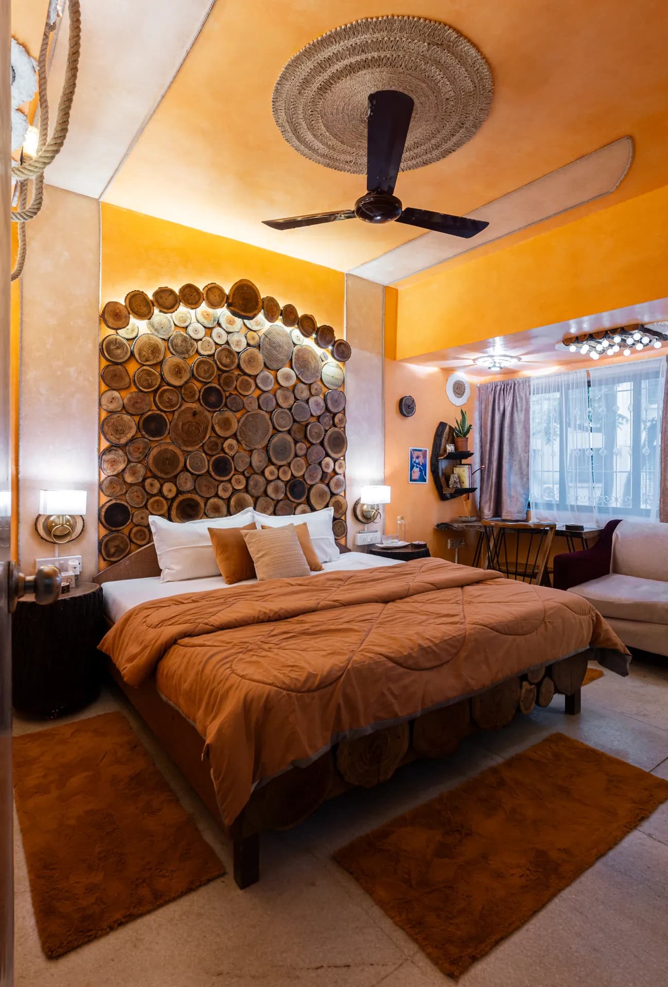 Bedroom with a king bed under a wood-slice headwall, orange walls, and a woven-rattan ceiling fan.