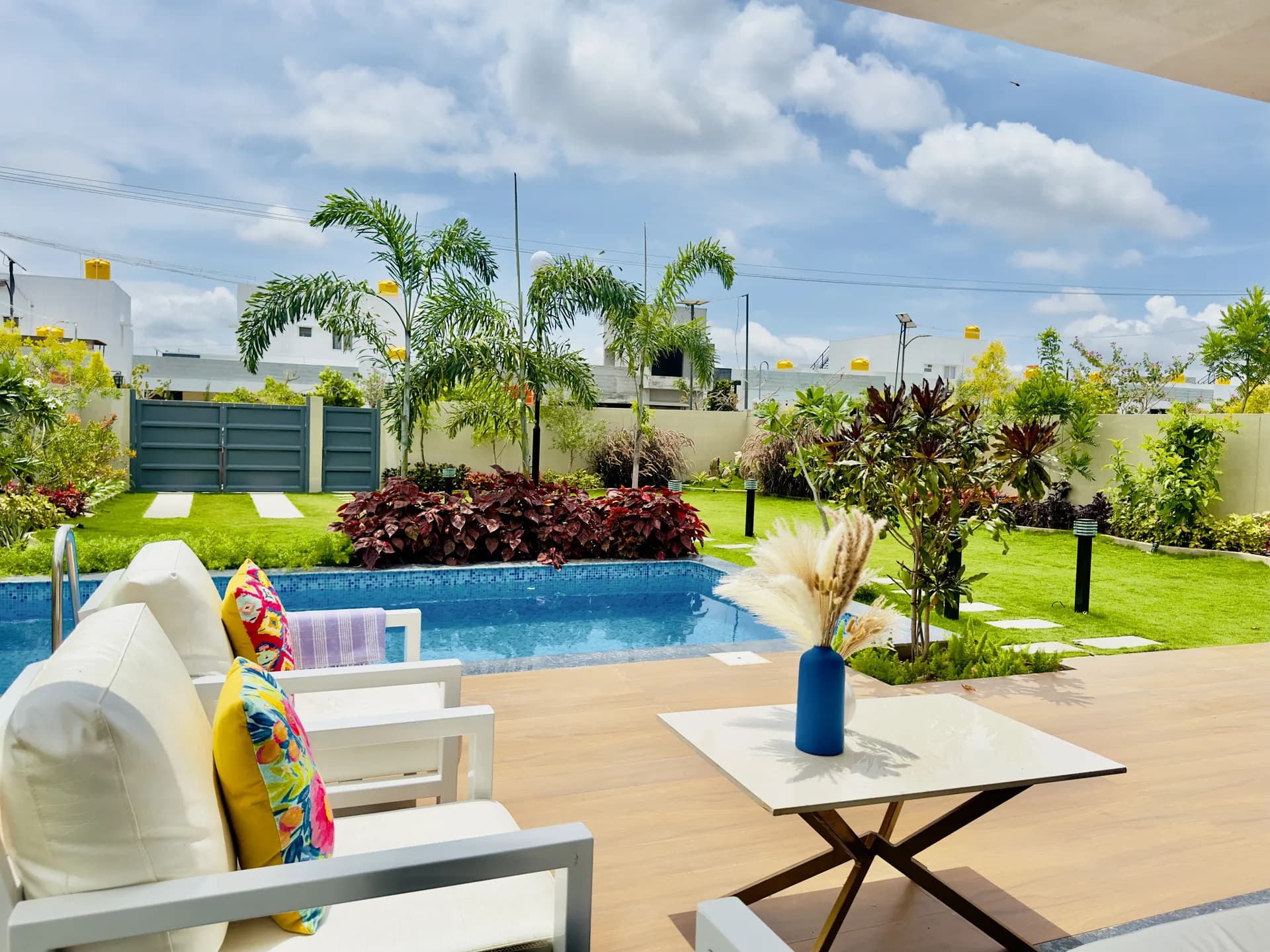 Outdoor terrace beside a blue-tiled pool, with white lounge chairs, a coffee table and a lawn beyond.