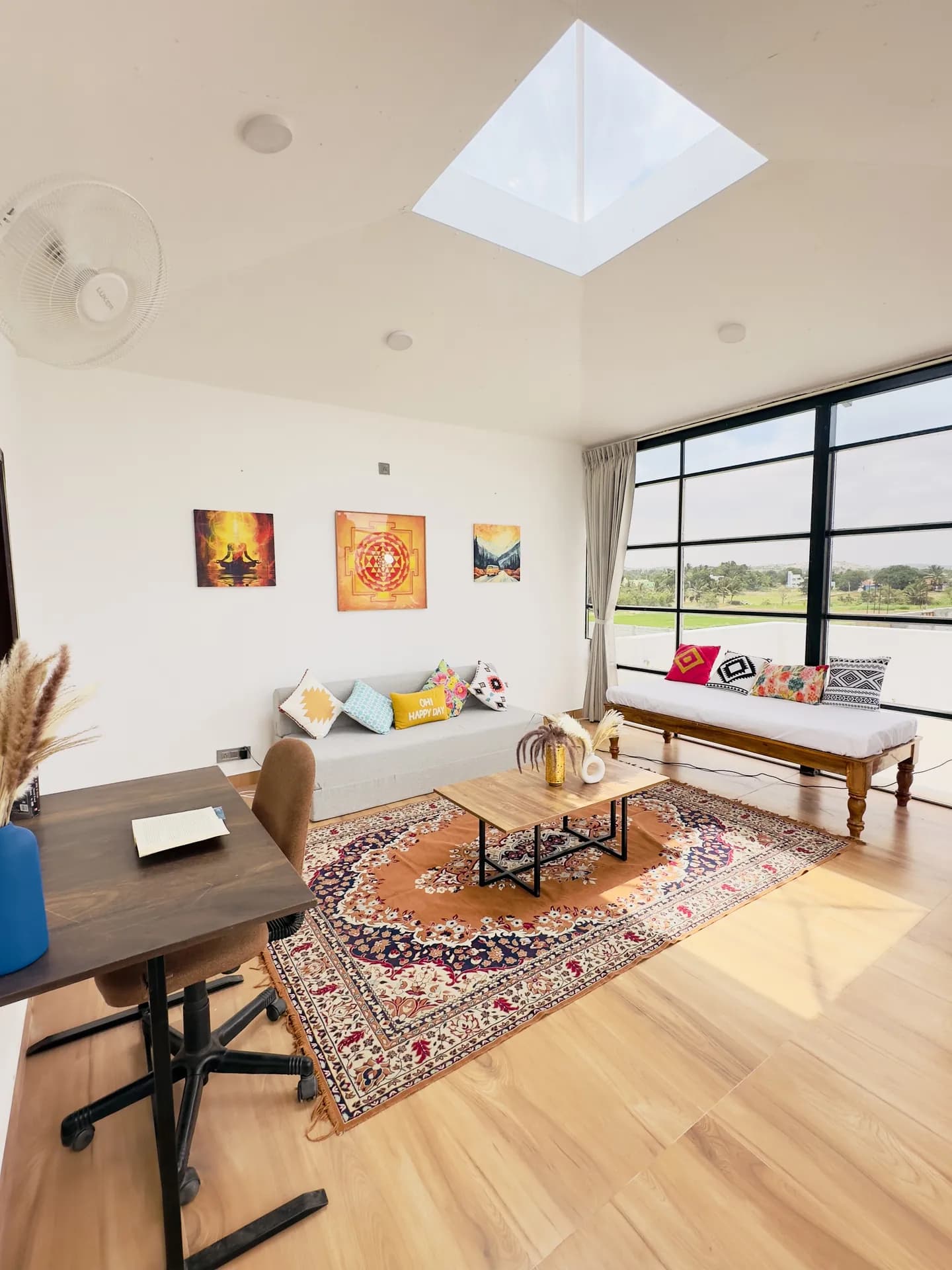 Bright living room with a skylight, large black-framed windows, a low sofa and a wooden daybed under a patterned rug.