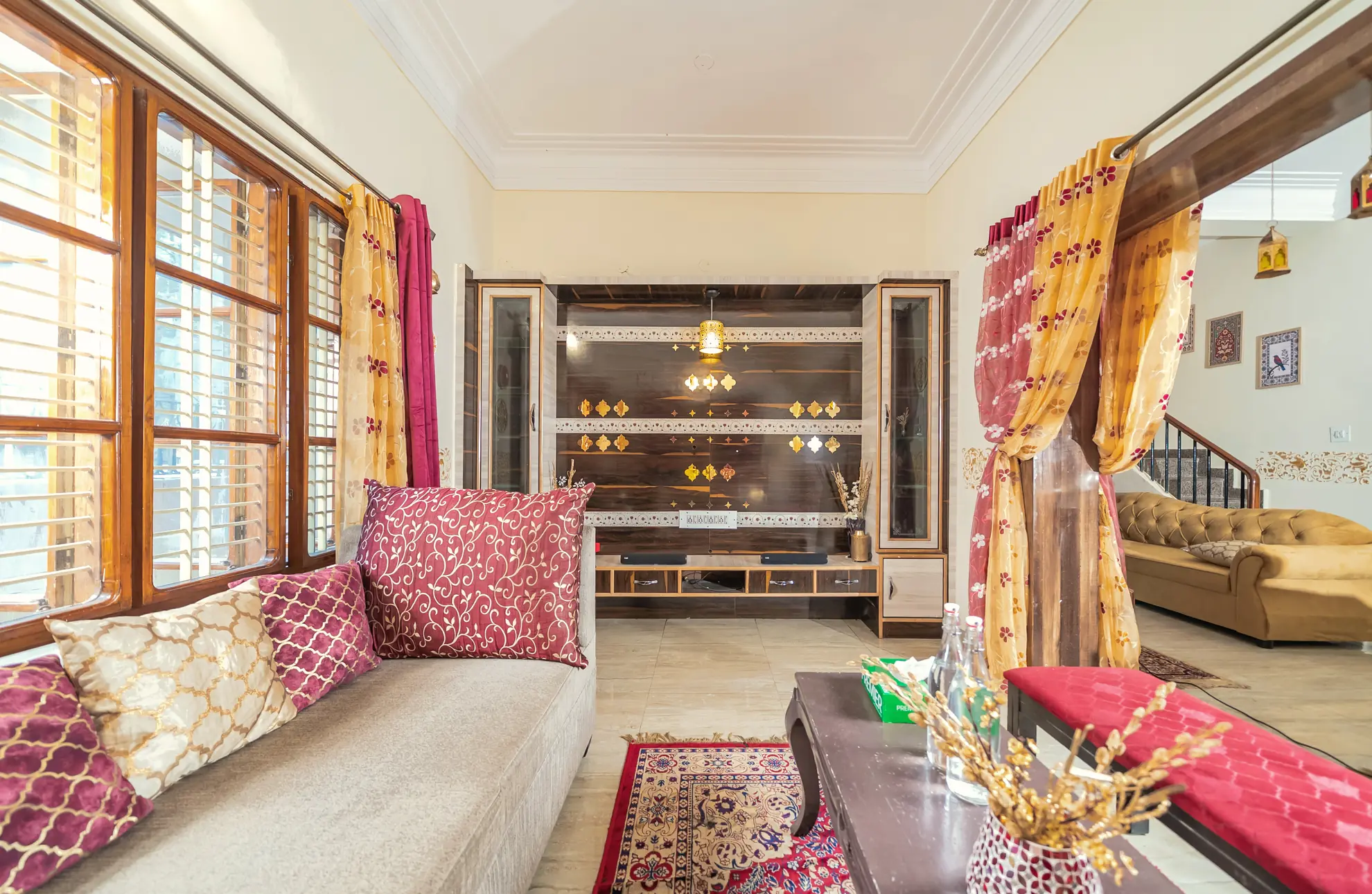 Living room with cream sofa, patterned cushions, carved wooden wall unit, and a low wooden coffee table on a rug.