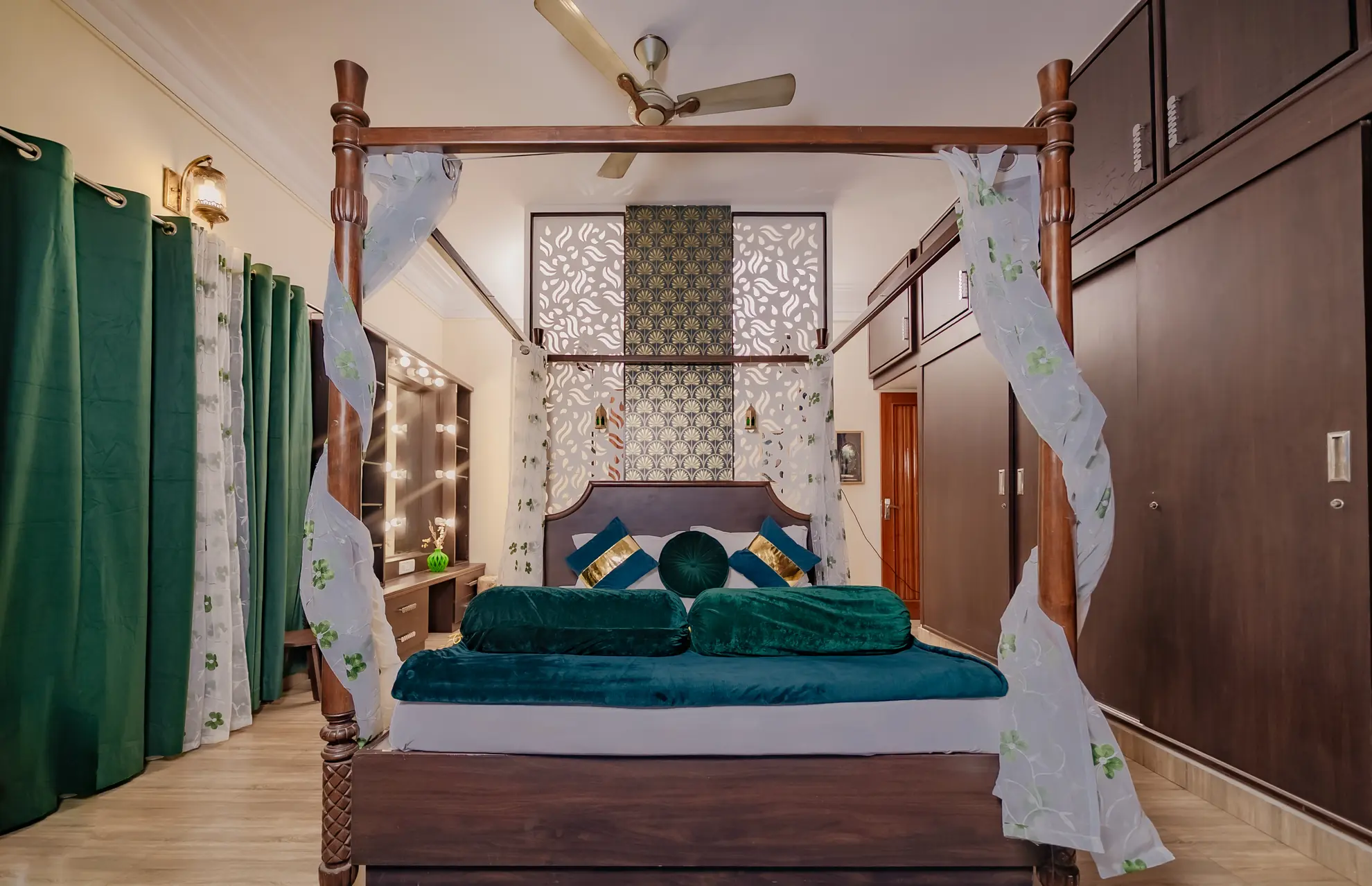 Bedroom with a four-poster bed dressed in green velvet, green curtains, and a built-in dressing table with bulbs.