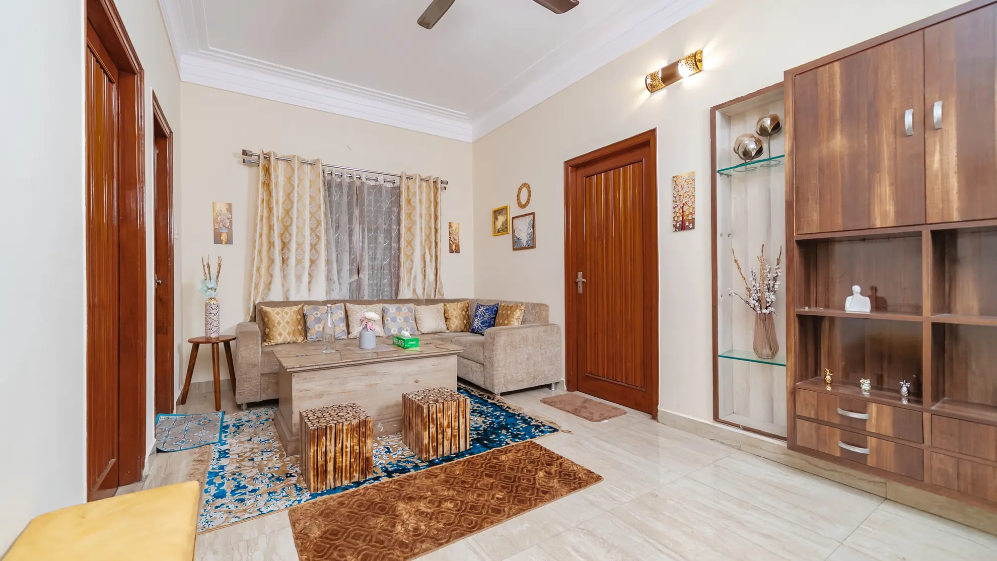 Living room with beige sectional sofa, wooden coffee table, patterned rugs and a tall wooden display cabinet.