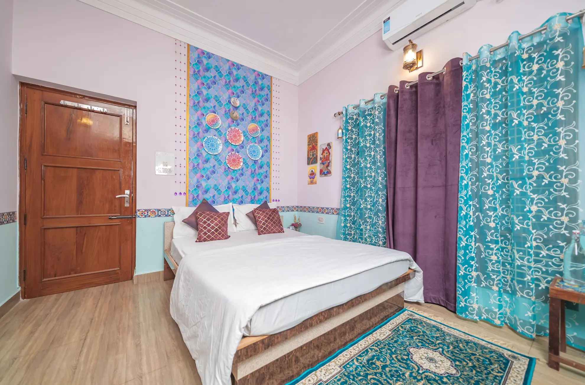 Bedroom with a double bed, blue patterned wall panel, turquoise sheer curtains and a wall-mounted air conditioner.