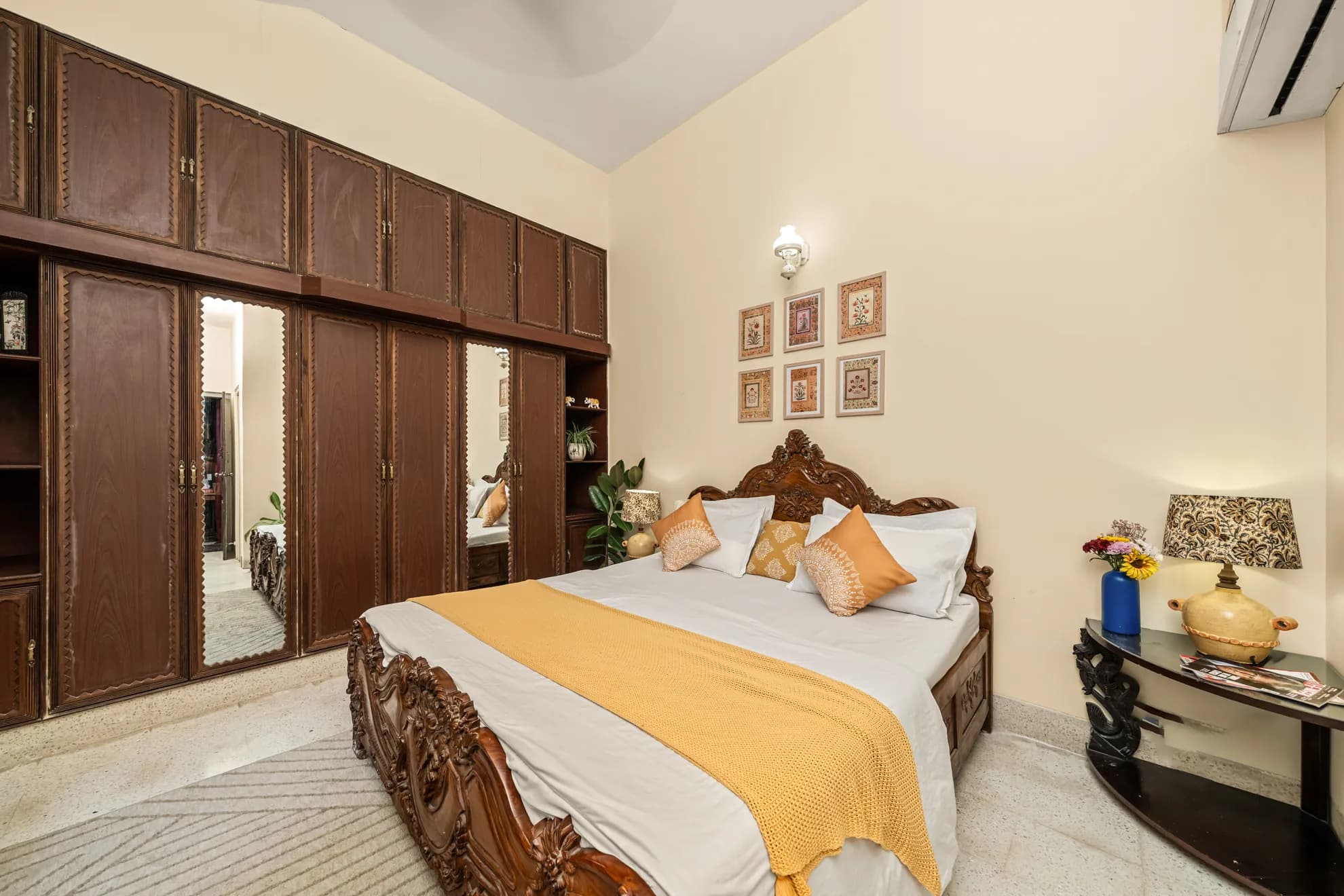 Bedroom with a carved wooden double bed, built-in wardrobes with mirrored doors, and a wall-mounted air conditioner.