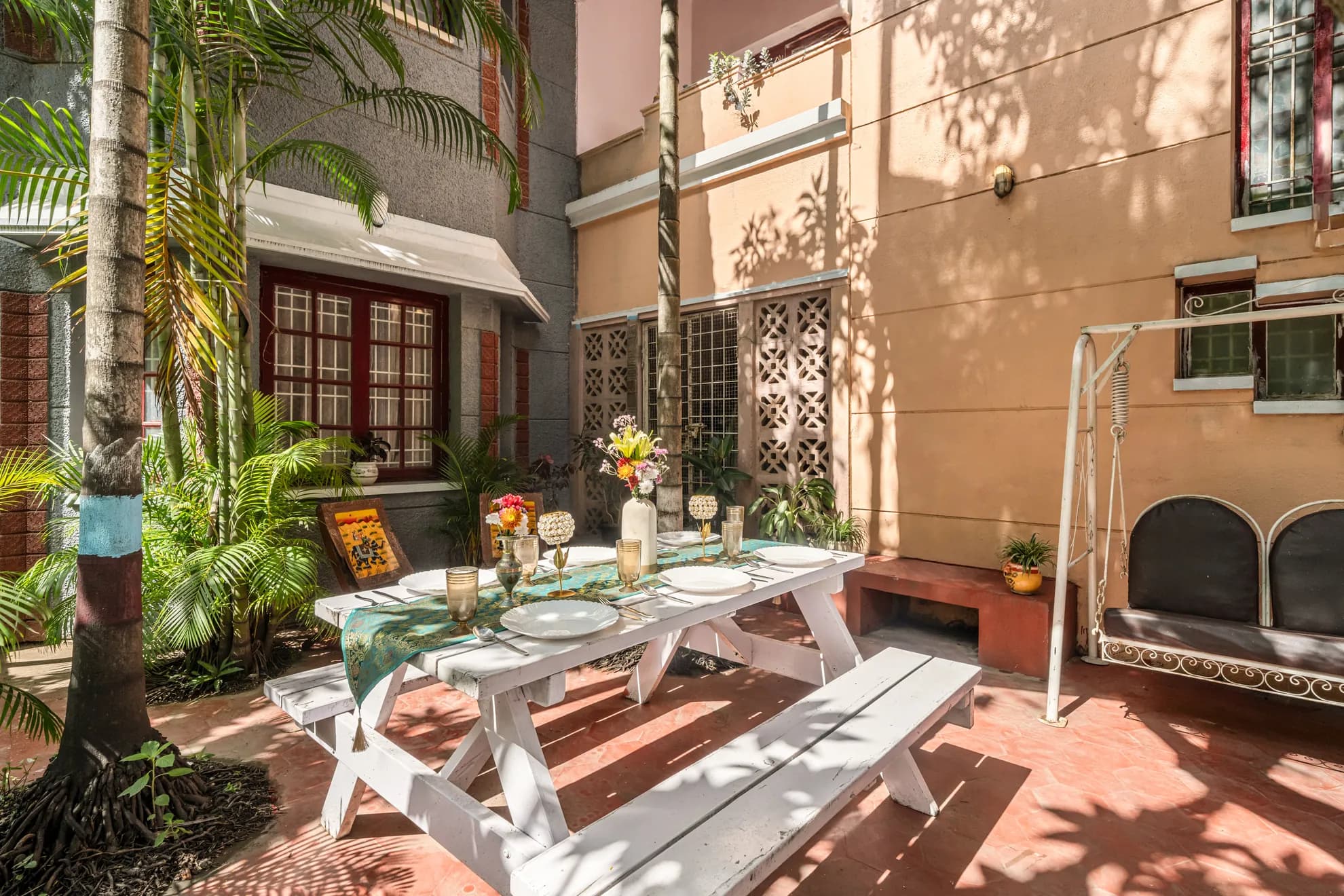 Courtyard patio with a white wooden picnic table set for a meal, a swing bench, and palm trees.