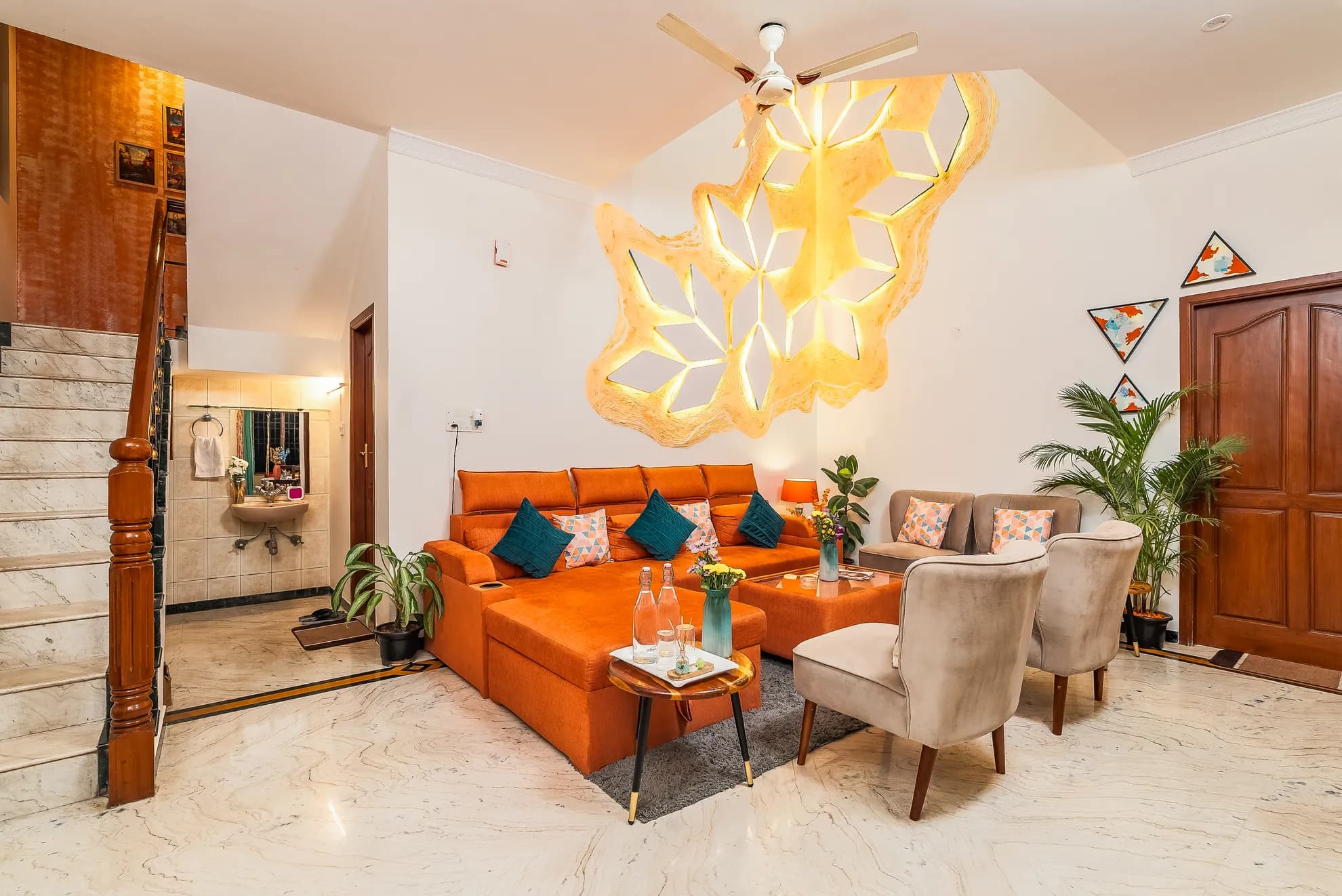 Living room with an orange sectional sofa, a glowing geometric pendant light, and marble floors.