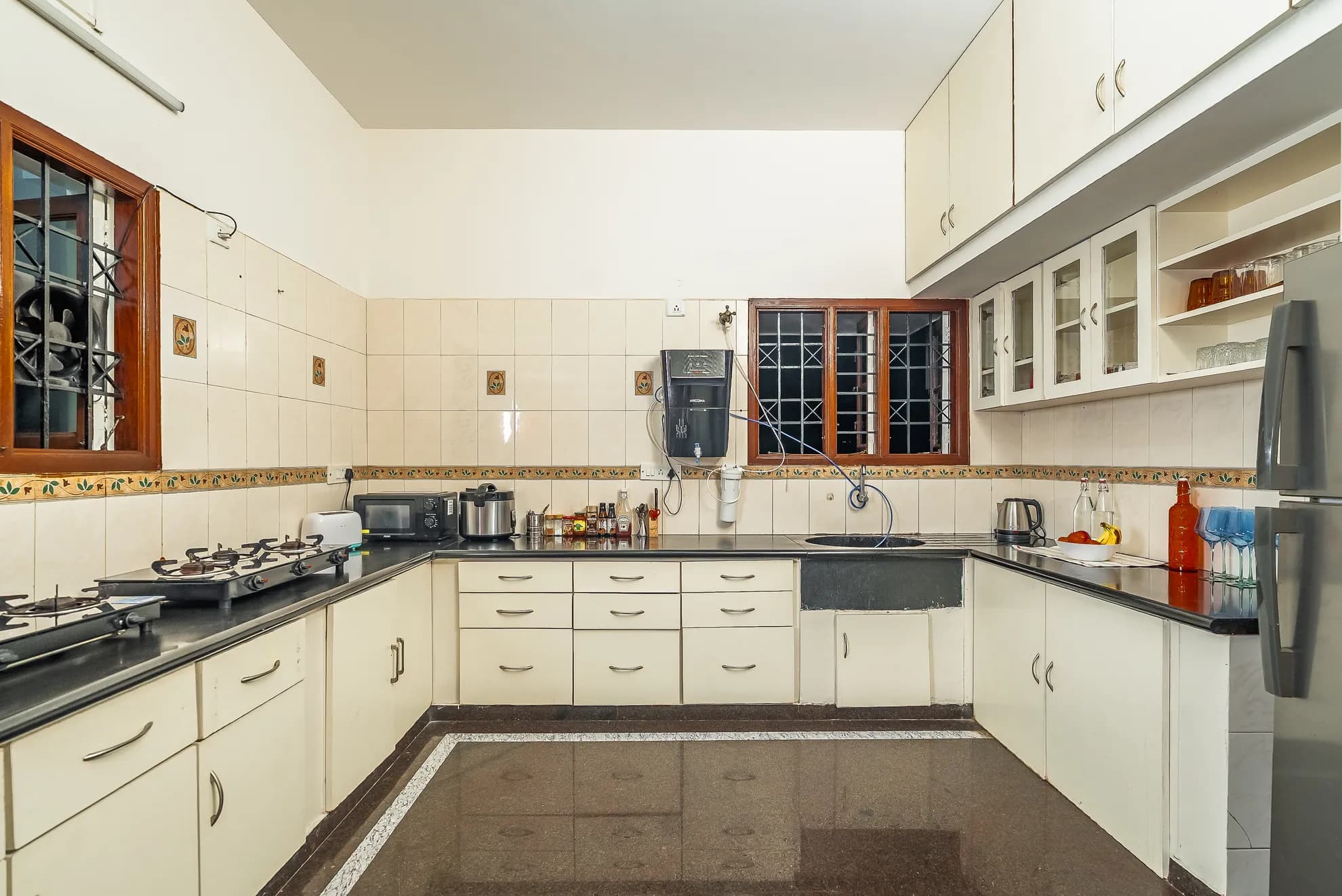 Galley-style kitchen with cream cabinets, black countertops, a gas hob, microwave and steel refrigerator.