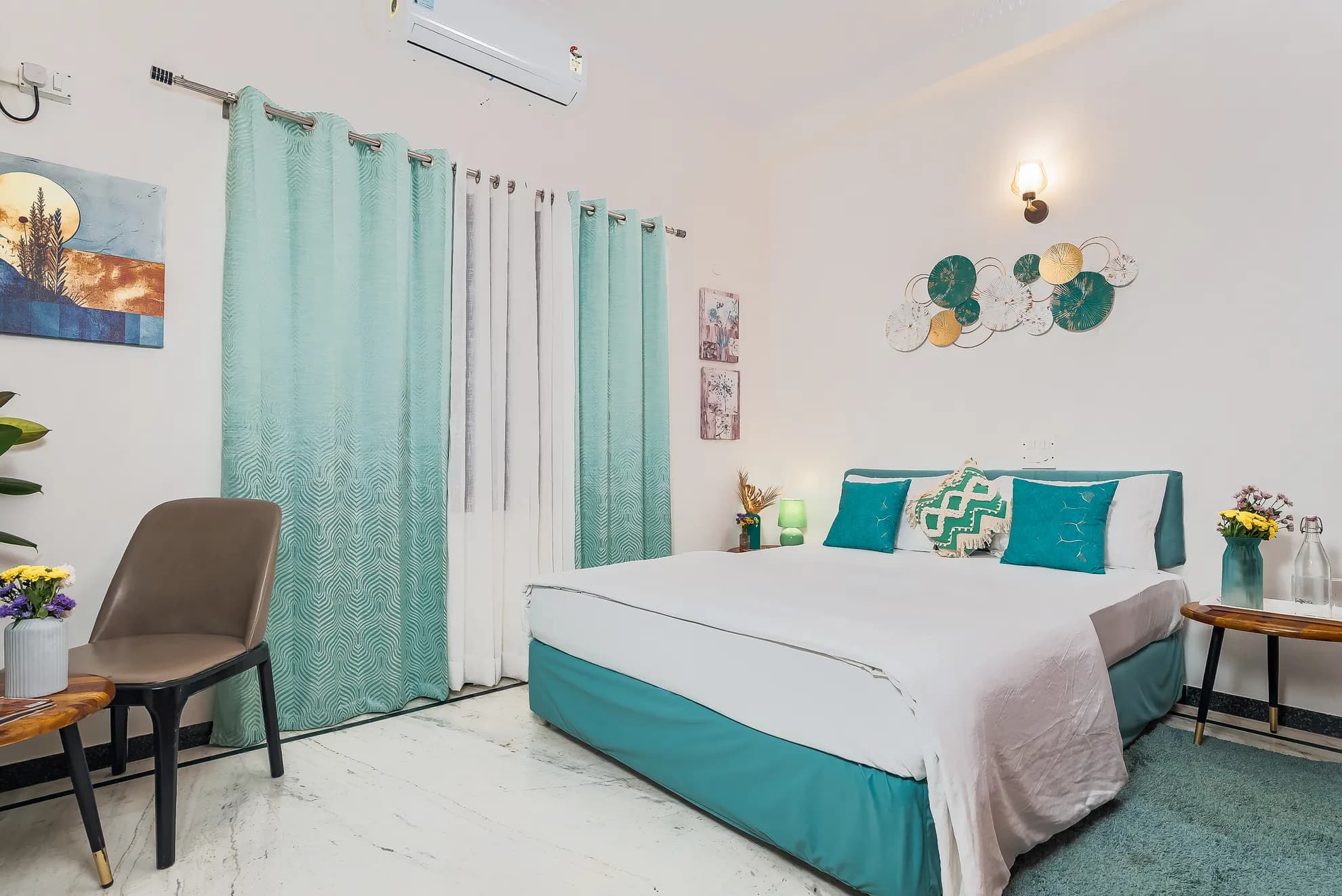 Bedroom with a made-up king bed, teal curtains, wall art and a small wall sconce light.