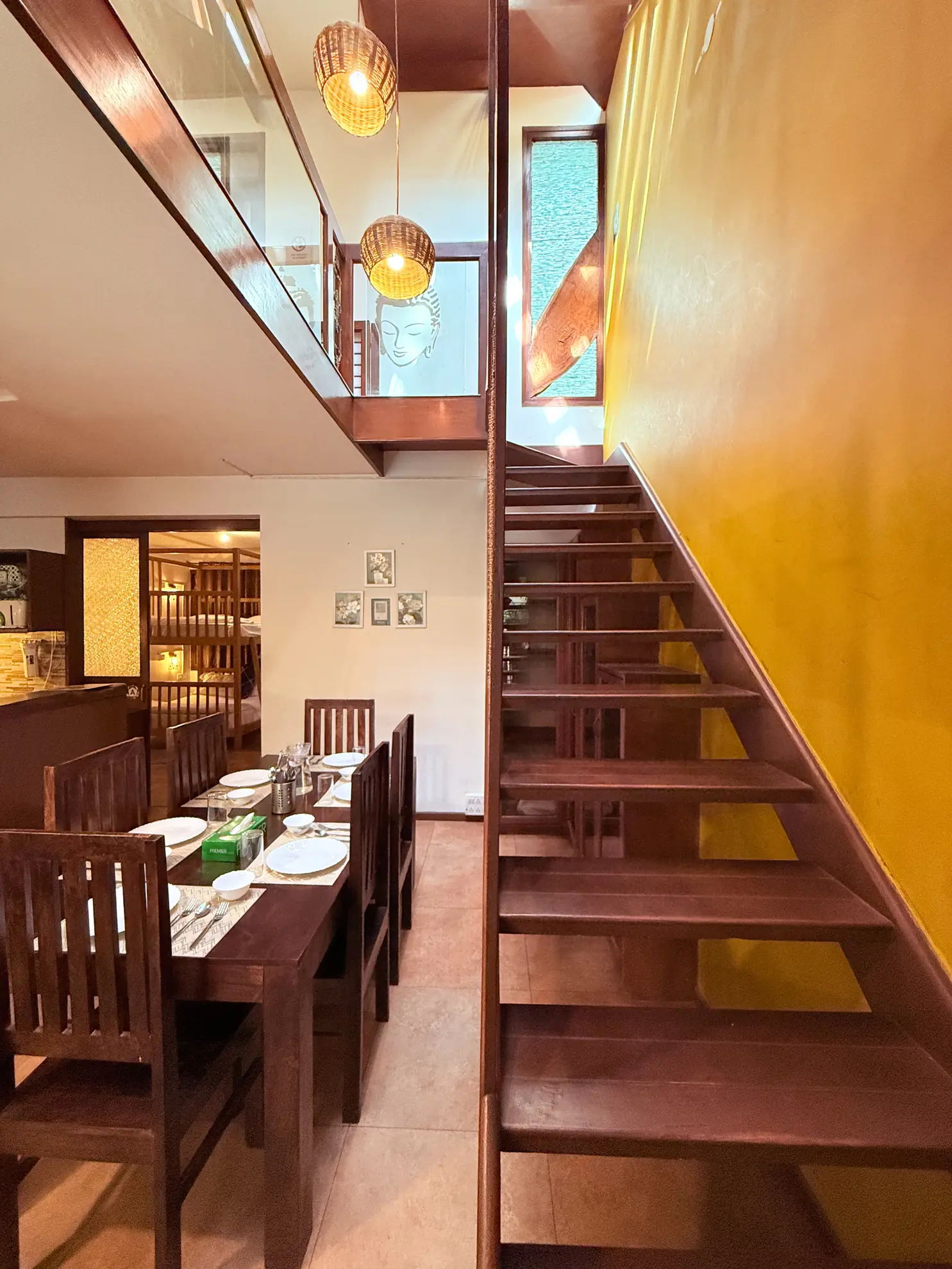 Dining area with a wooden table set for four, a staircase with dark wood treads, and a Buddha face mural.
