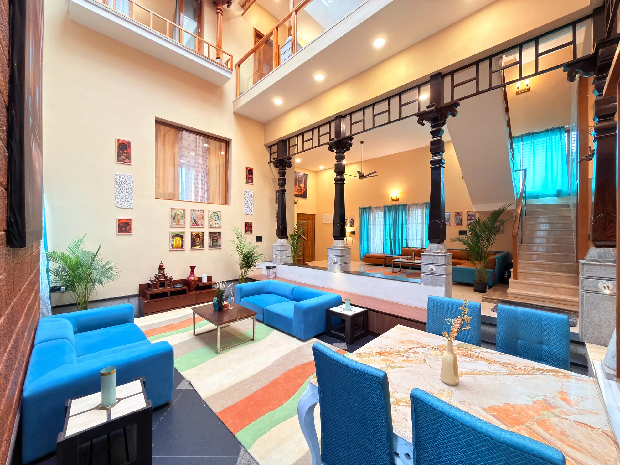 Double-height living room with blue sofas, a stone-topped dining table and dark wooden columns under a skylight.