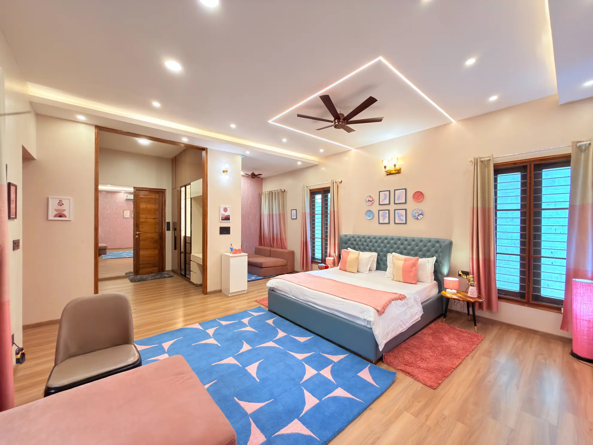 Bright bedroom with a teal upholstered bed, blue geometric rug, and ceiling fan under lit cove ceiling.