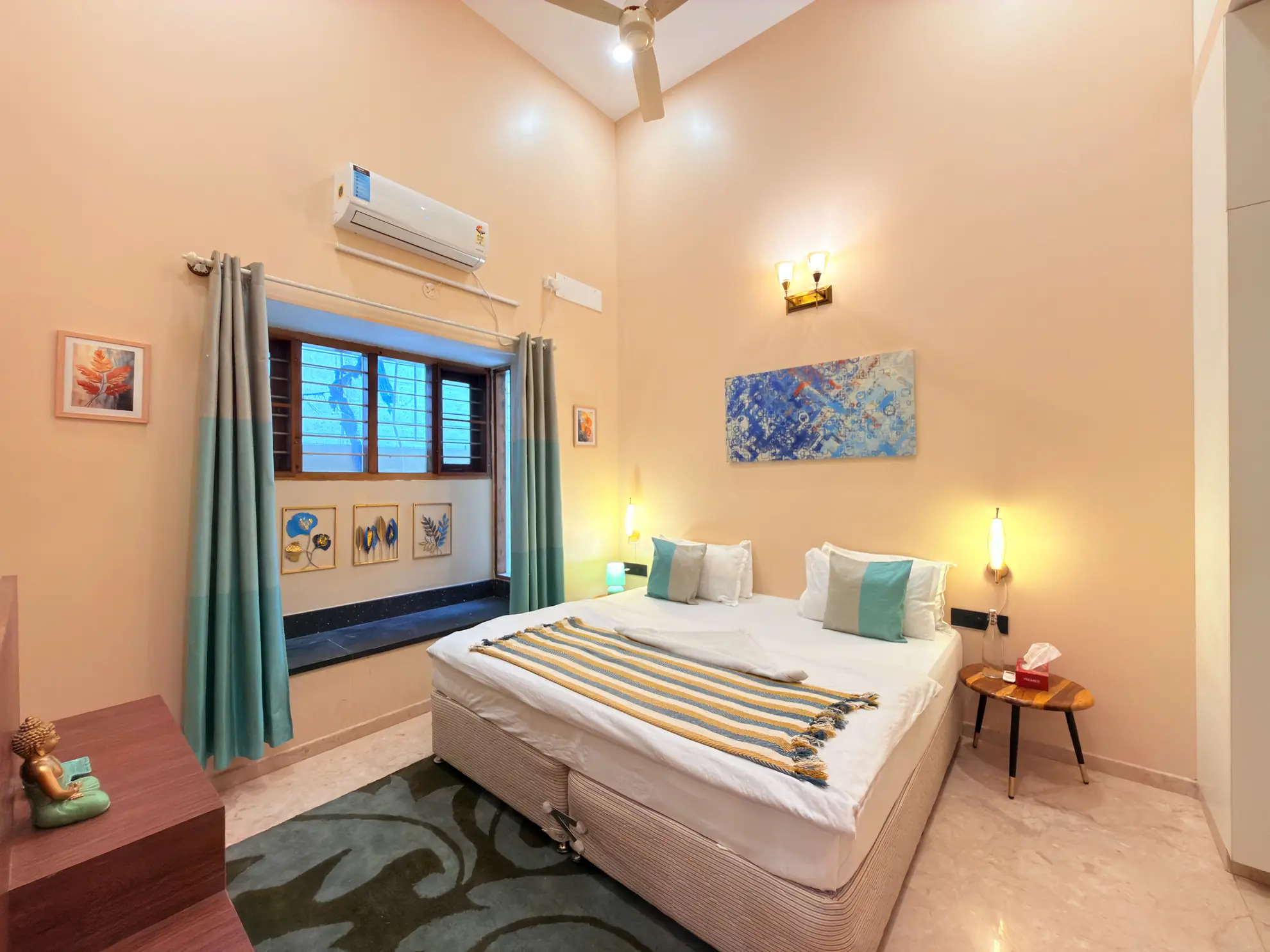 Bedroom with a made-up double bed, wall air conditioner, tall ceiling fan, and a window with teal curtains.