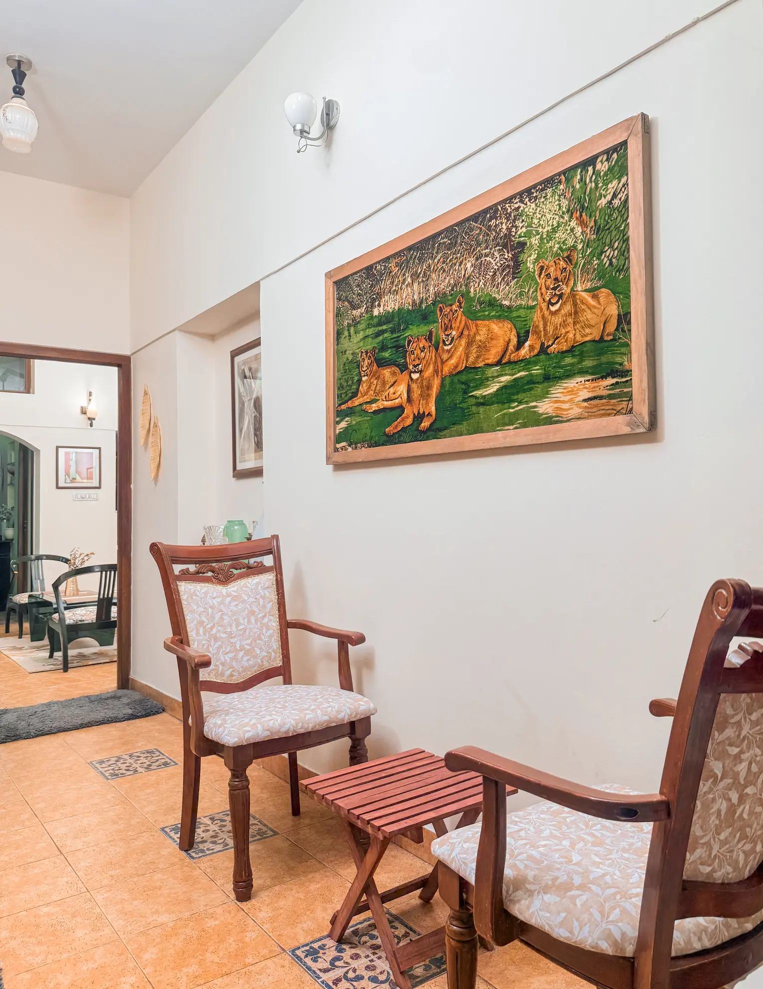 Foyer with two wooden armchairs, a small slatted side table, and a large framed painting of lions.