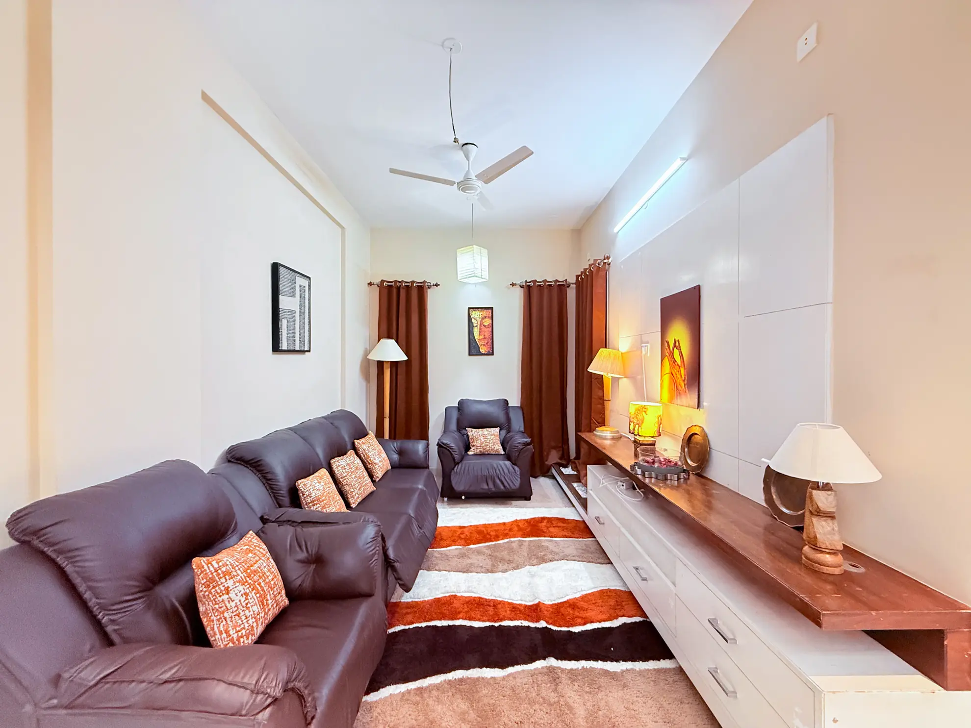 Living room with two brown leather sofas, striped rug, wall-mounted TV unit, and warm table lamps.