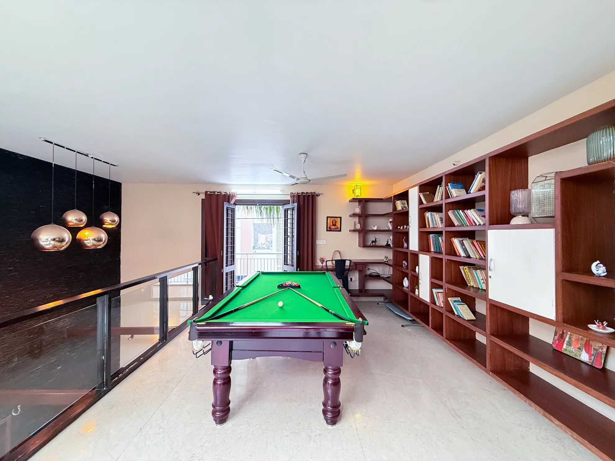 Upper-floor games room with a green pool table, a wall of wooden bookshelves, and copper pendant lights.