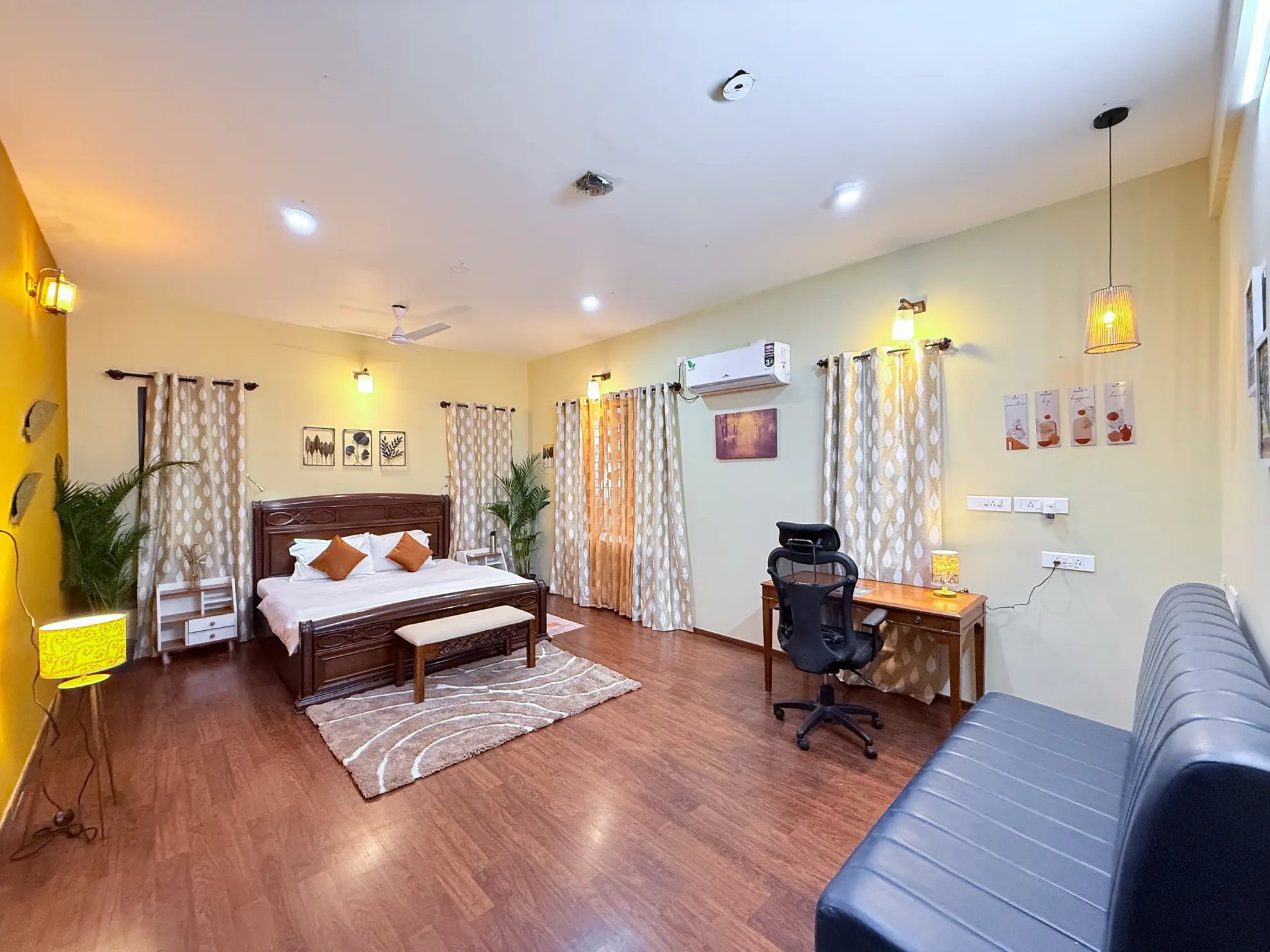 Bedroom with a wooden king bed, air conditioner, and a desk with office chair beside a sofa.