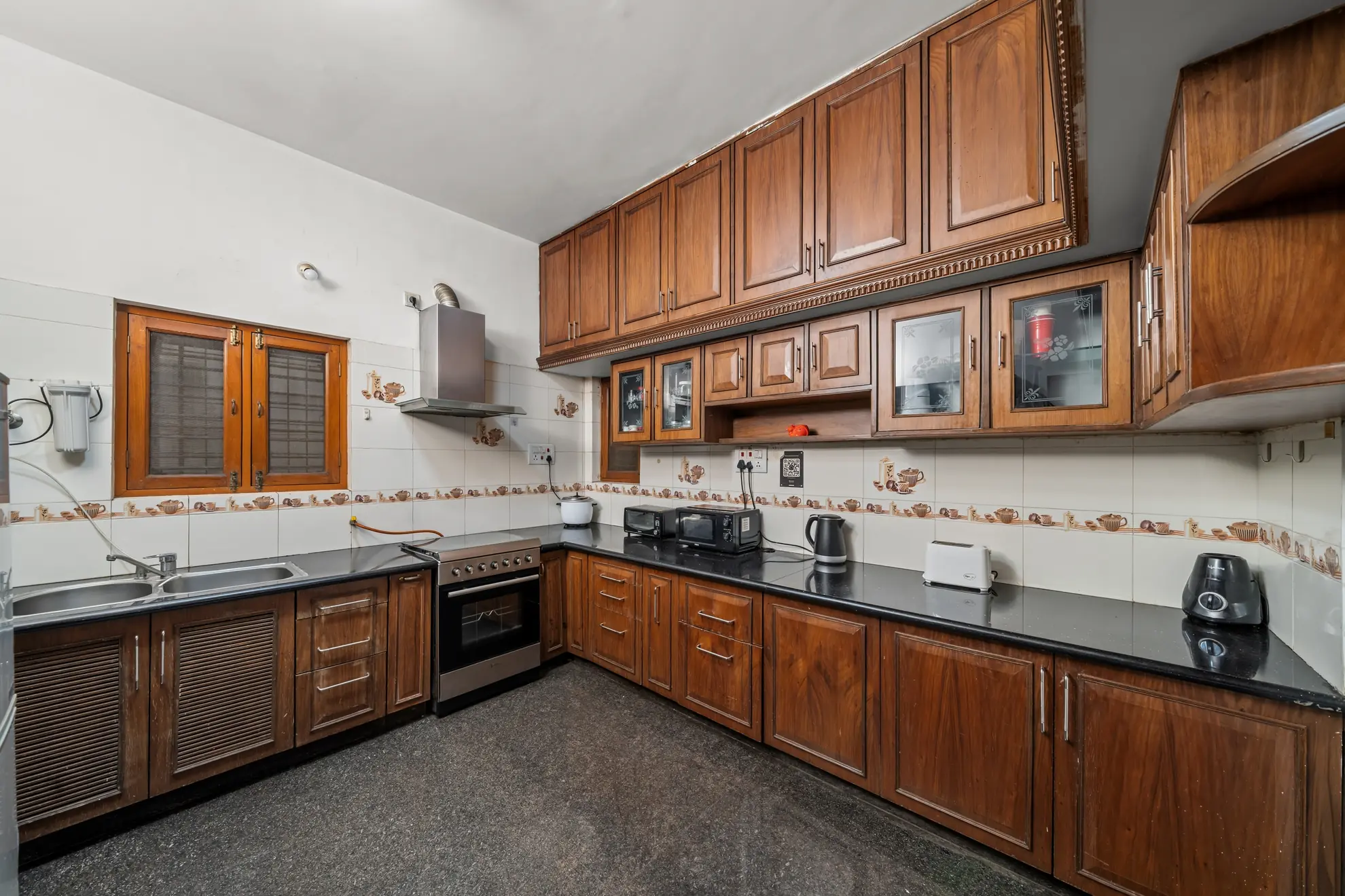Galley-style kitchen with dark wood cabinets, black countertops, a built-in oven, and a double sink by the window.