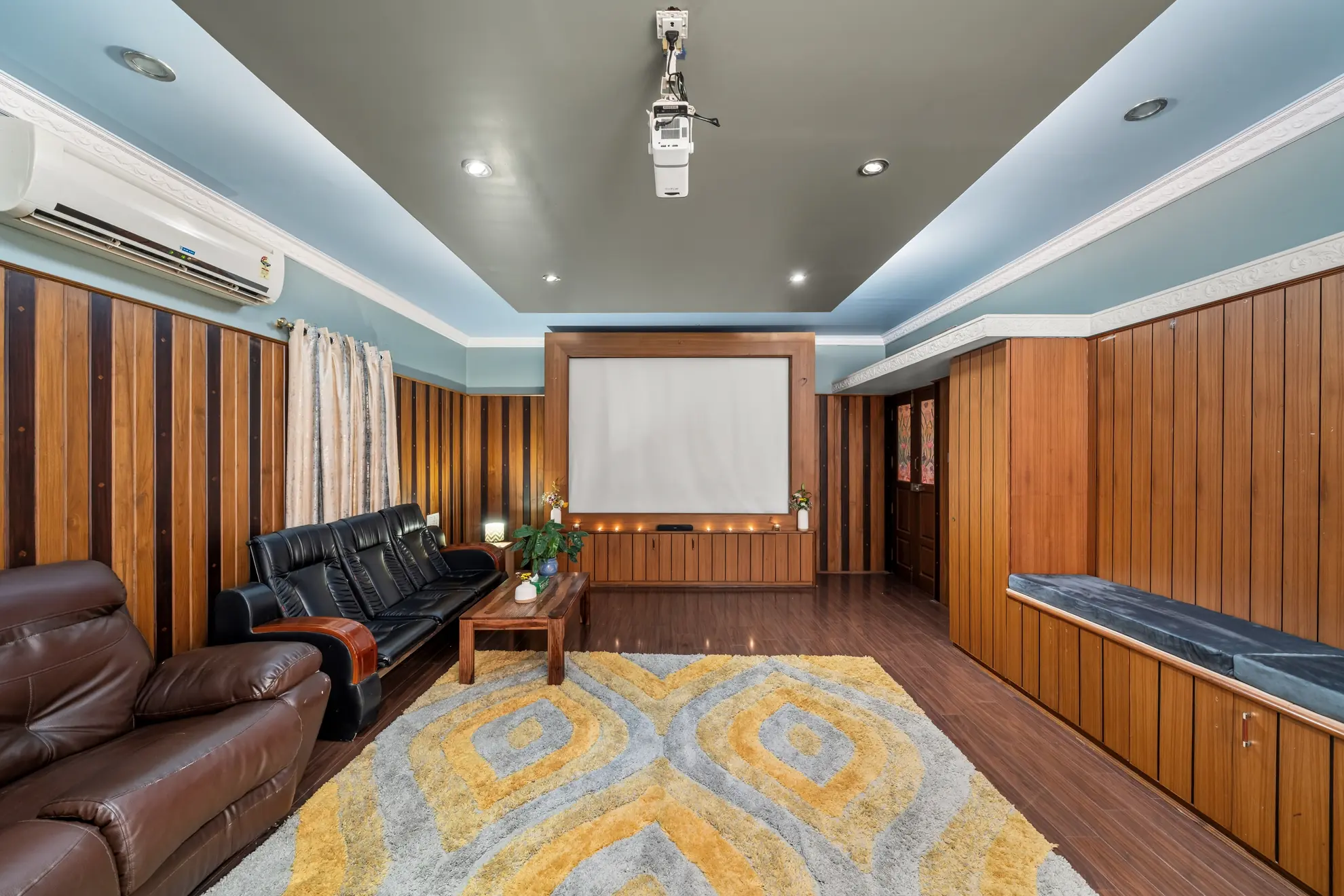 Wood-paneled home theatre with a projector, large screen, leather recliners and a built-in bench seat.