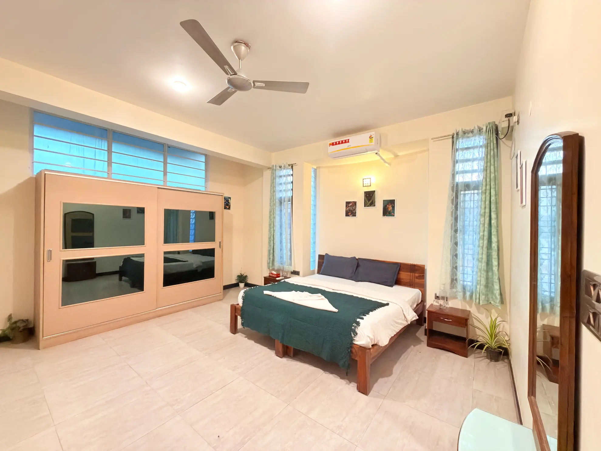 Bedroom with a double bed, green throw, wall-mounted air conditioner, ceiling fan and large wooden wardrobe.