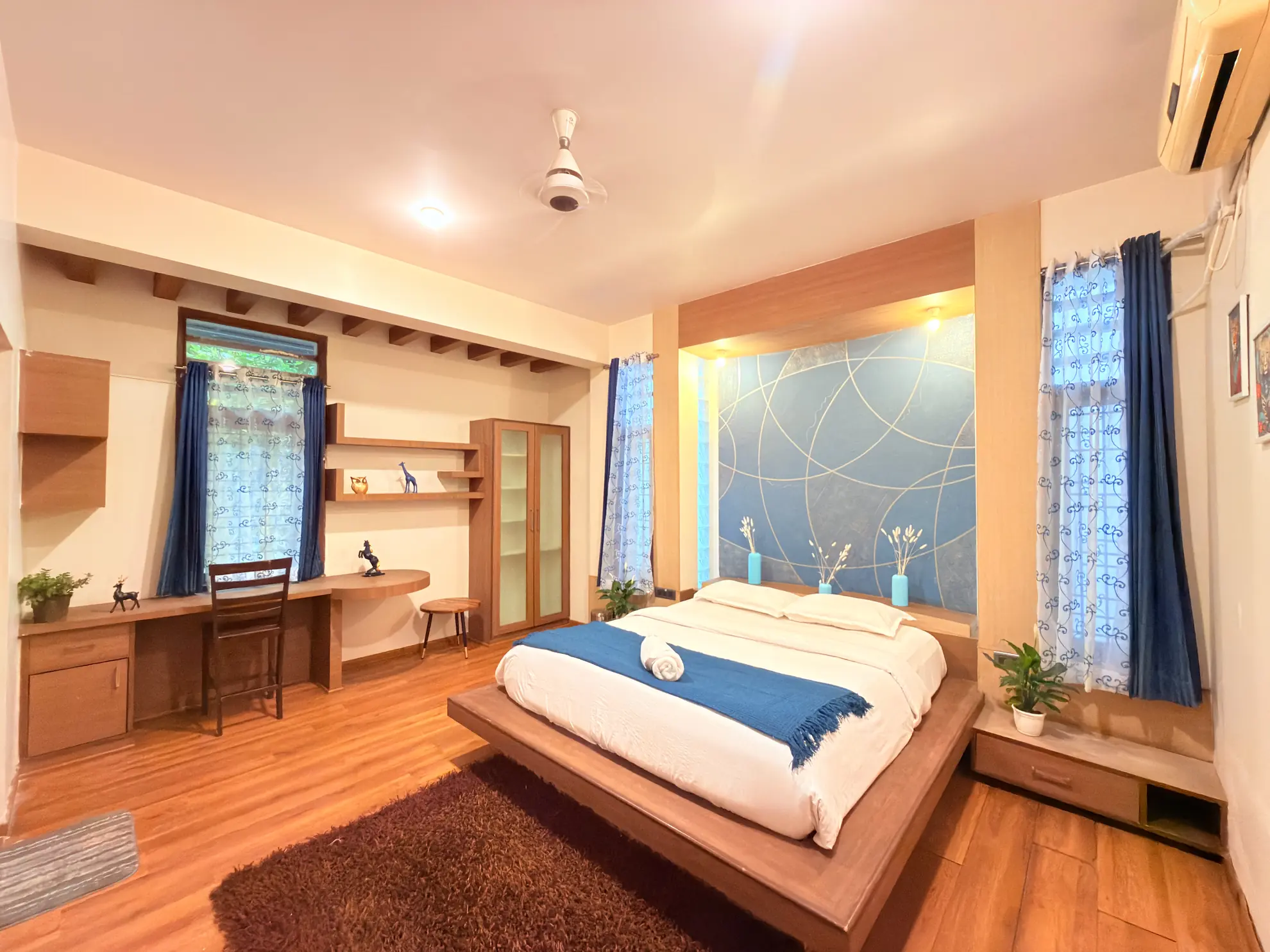 Bedroom with a platform bed, blue accent wall, built-in desk and wardrobe, and wooden floors.