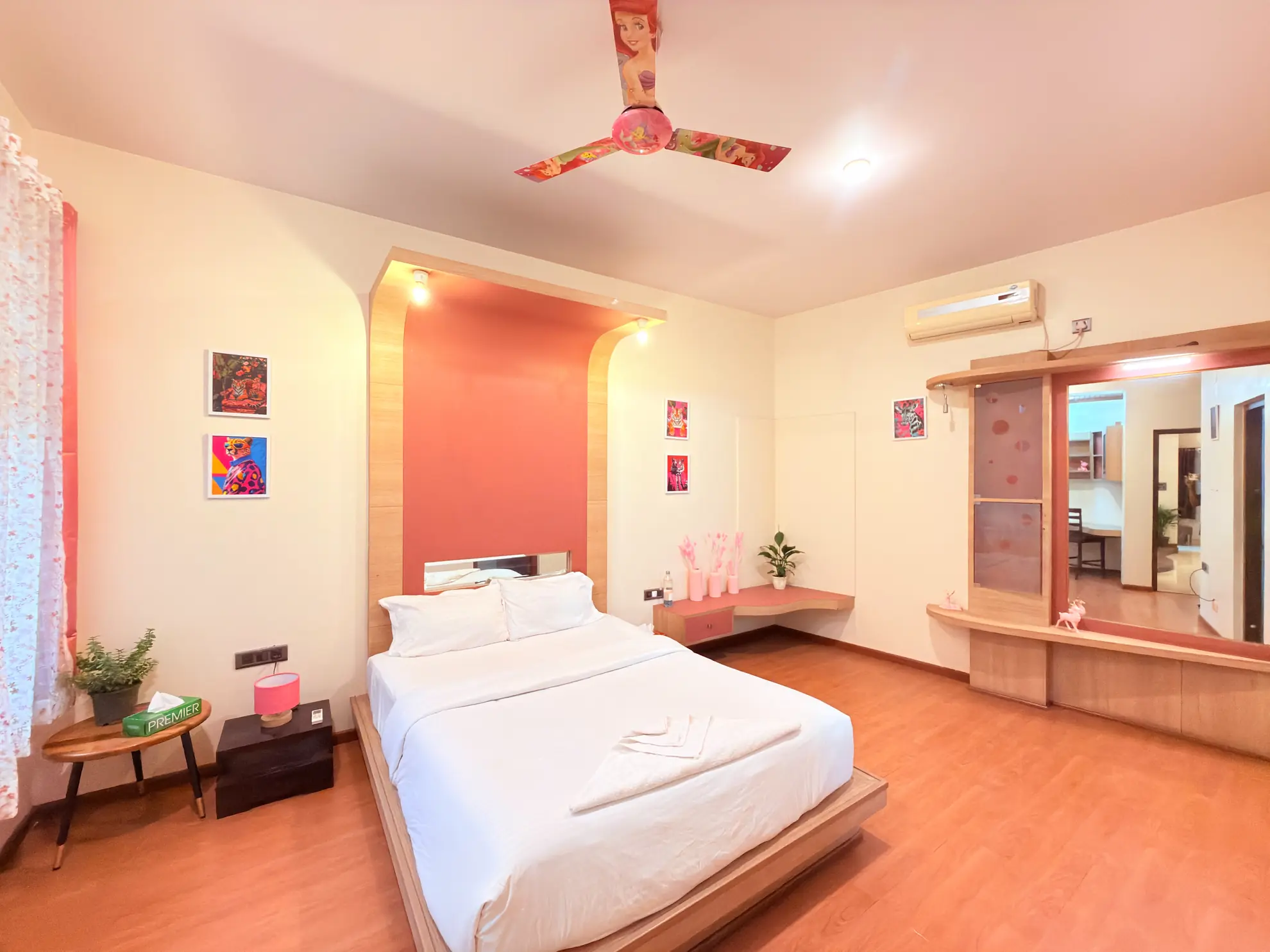 Bedroom with a double bed, pink-accented feature wall, wall-mounted air conditioner and a dressing mirror unit.