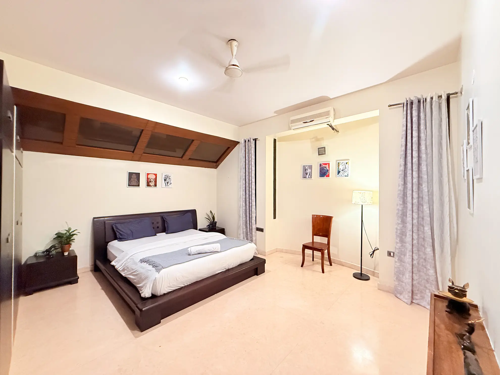 Bedroom with a low dark wood platform bed, wall-mounted air conditioner, and sheer curtains by a large window.